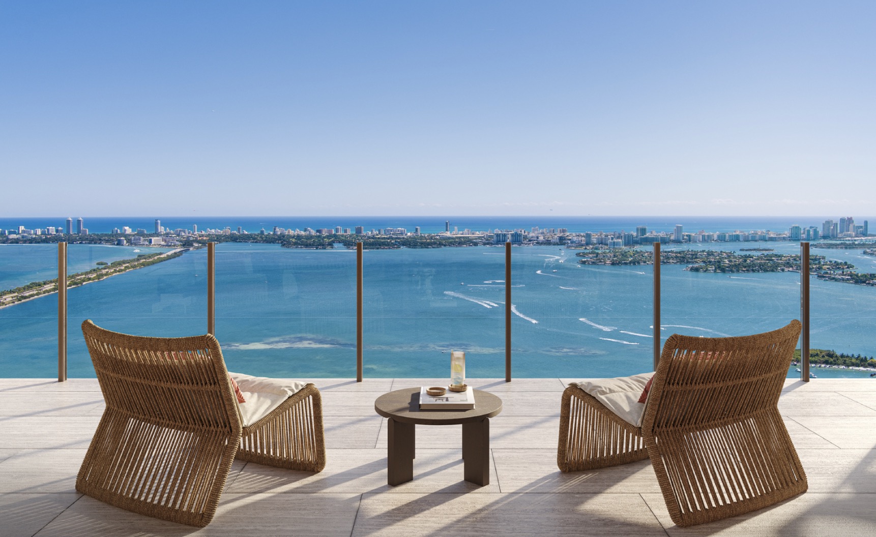 This image showcases a luxurious balcony with stunning panoramic views of the ocean and city skyline. Two modern woven chairs and a small round table create an inviting outdoor seating area. The glass railing provides an unobstructed view, enhancing the sense of openness and sophistication.
