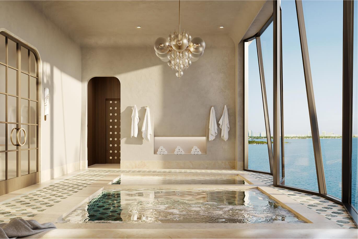 This luxurious primary bathroom features a unique spa-like design with multiple soaking pools and floor-to-ceiling windows offering stunning ocean views. The room is adorned with a modern chandelier, neutral tones, and elegant tile work, creating a serene and upscale atmosphere. Towels are neatly hung, and the space is well-lit, emphasizing the high-end finishes and architectural details.