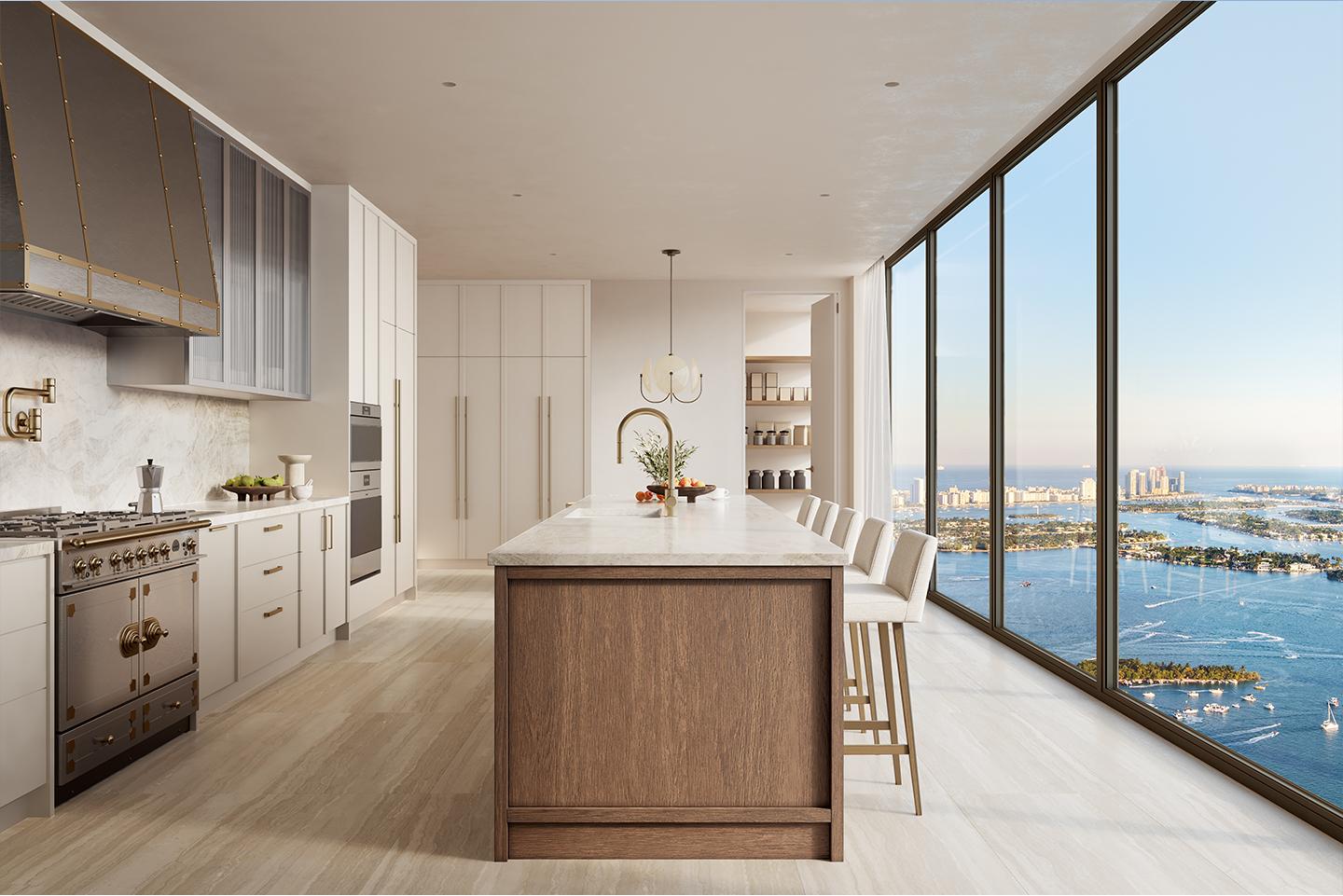 This is a bright and modern kitchen with a large island, high-end appliances, and floor-to-ceiling windows offering stunning ocean views. The kitchen features a mix of white and wood cabinetry, marble countertops, and brass accents, creating a luxurious and inviting space. The perspective is from the side, showcasing the island and the view.