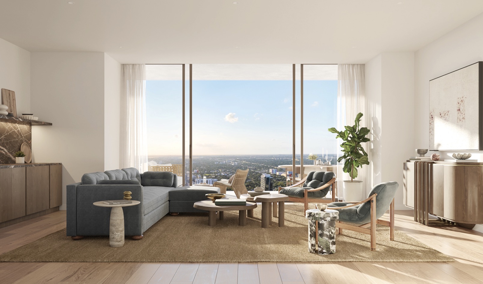 This is a bright and airy living room with floor-to-ceiling windows offering a stunning city view. The room features a comfortable gray sectional sofa, two stylish armchairs, and a round coffee table arrangement on a neutral-toned rug. The space is decorated with modern art and a large potted plant, creating a sophisticated and inviting atmosphere.