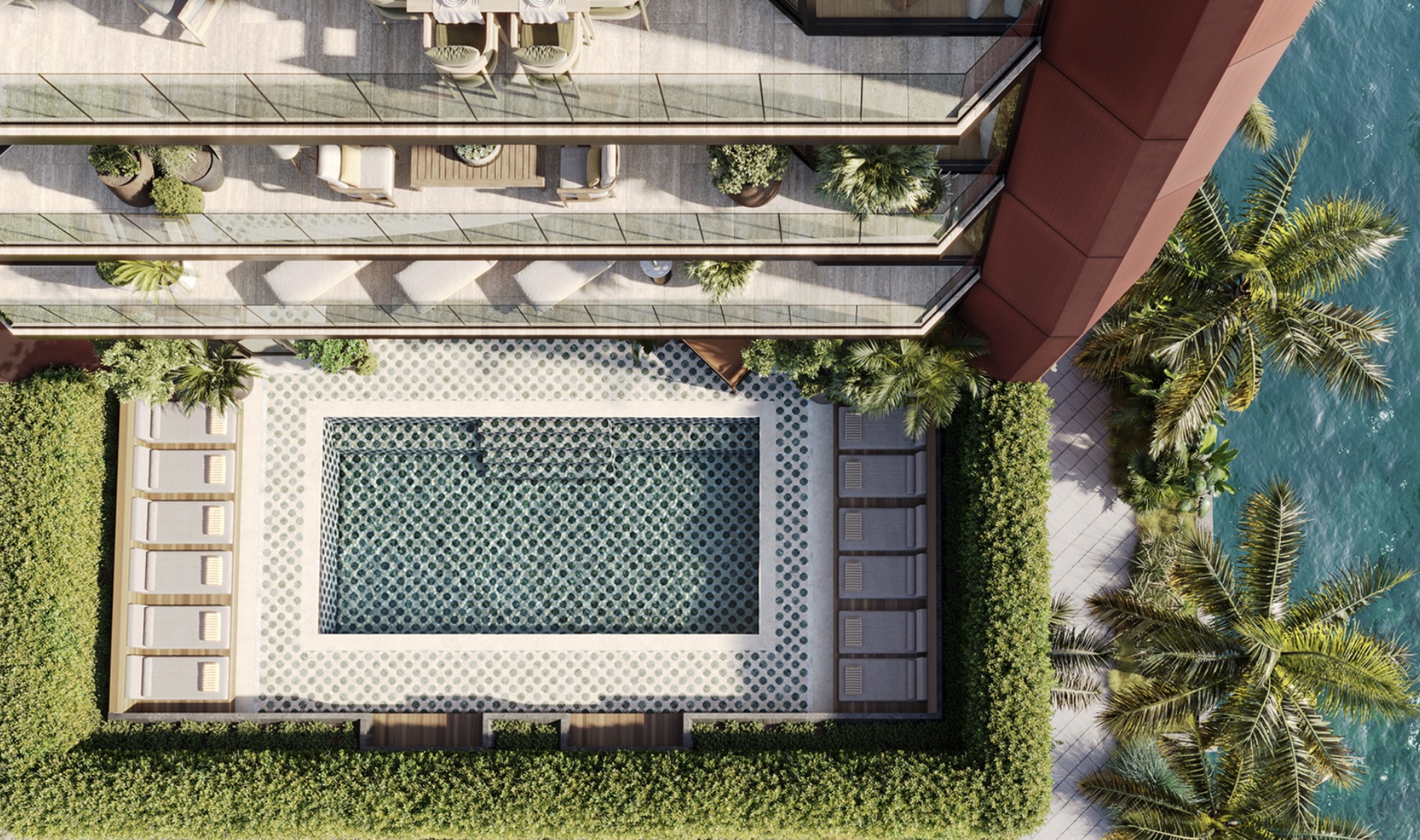 This aerial view showcases a luxurious outdoor space featuring a rectangular pool with patterned tiling, surrounded by lounge chairs and lush greenery. Balconies with outdoor seating extend from the building, offering views of the adjacent water. The overall impression is one of upscale relaxation and sophisticated design.