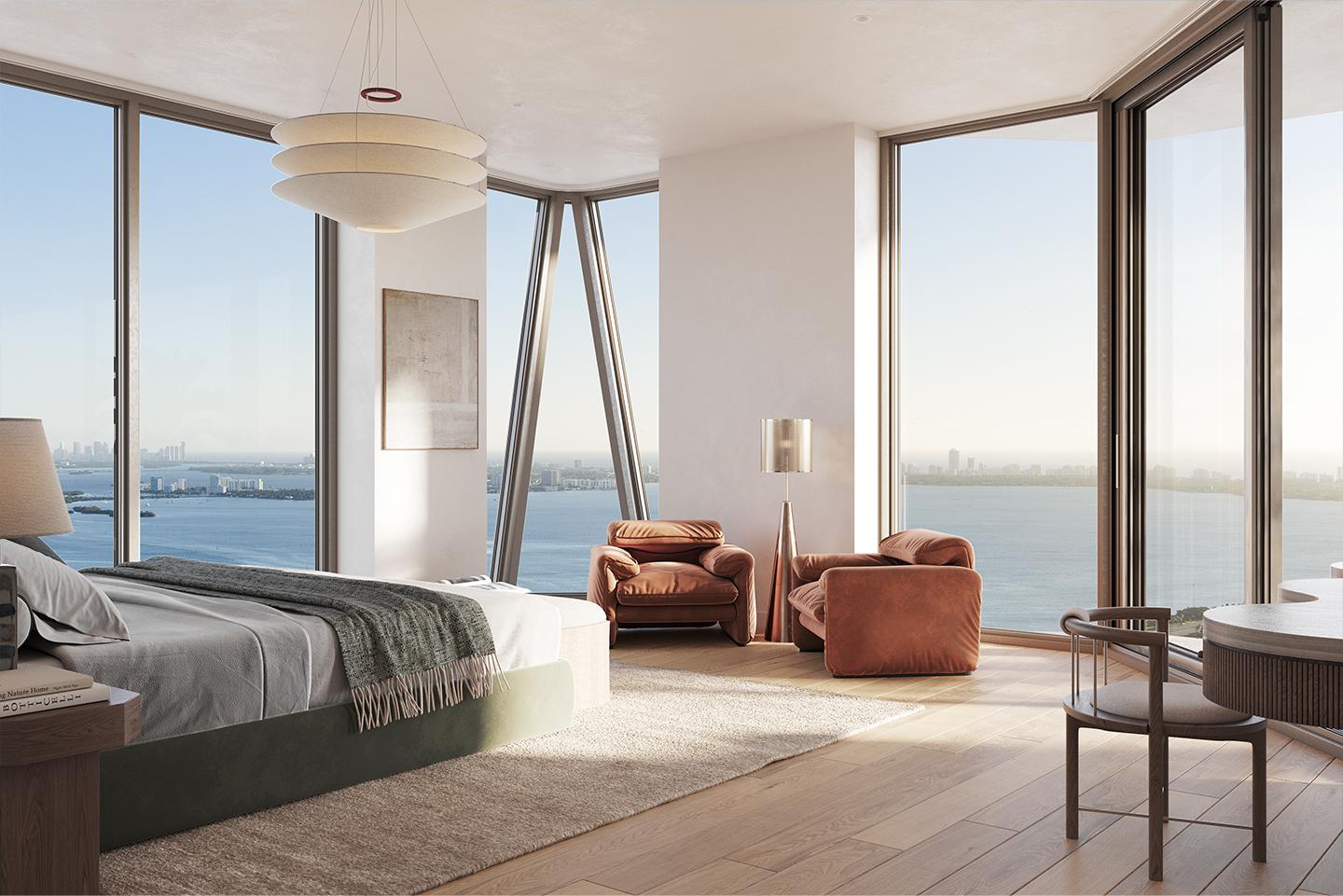 This is a luxurious primary bedroom featuring floor-to-ceiling windows with stunning water views. The room is furnished with a large bed, two comfortable armchairs, and a modern desk area. A unique pendant light fixture hangs above, adding to the room's elegant and contemporary style.