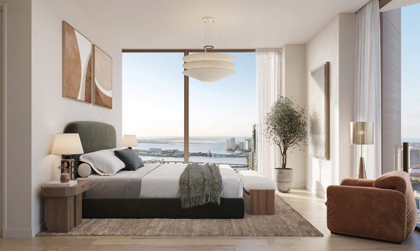This is a luxurious primary bedroom featuring a king-size bed with a green headboard, neutral bedding, and a cozy throw. The room boasts floor-to-ceiling windows offering stunning city and water views, complemented by modern art and stylish lighting fixtures. A comfortable armchair and a plush rug add to the room's inviting and sophisticated ambiance.