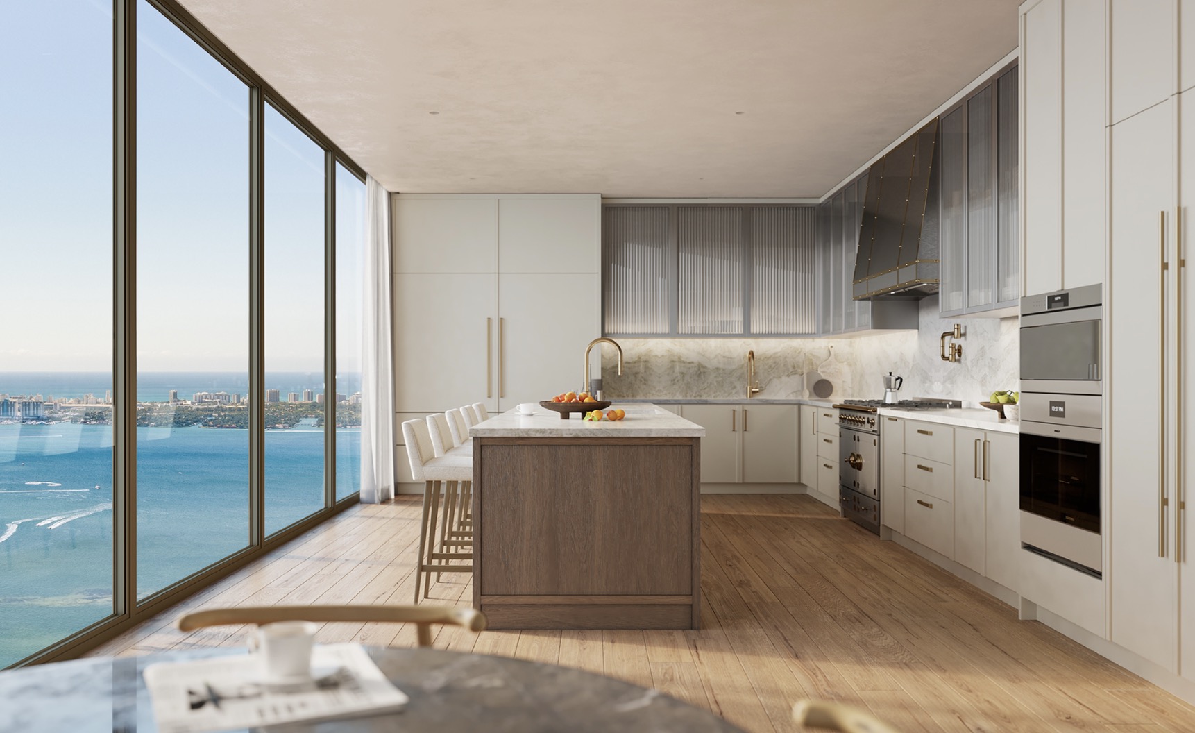 This is a bright and modern kitchen with a large island, light wood floors, and floor-to-ceiling windows offering a stunning ocean view. The kitchen features white and gray cabinetry, stainless steel appliances, and a marble backsplash, creating a luxurious and inviting space. The open layout and natural light enhance the overall appeal of this high-end kitchen.