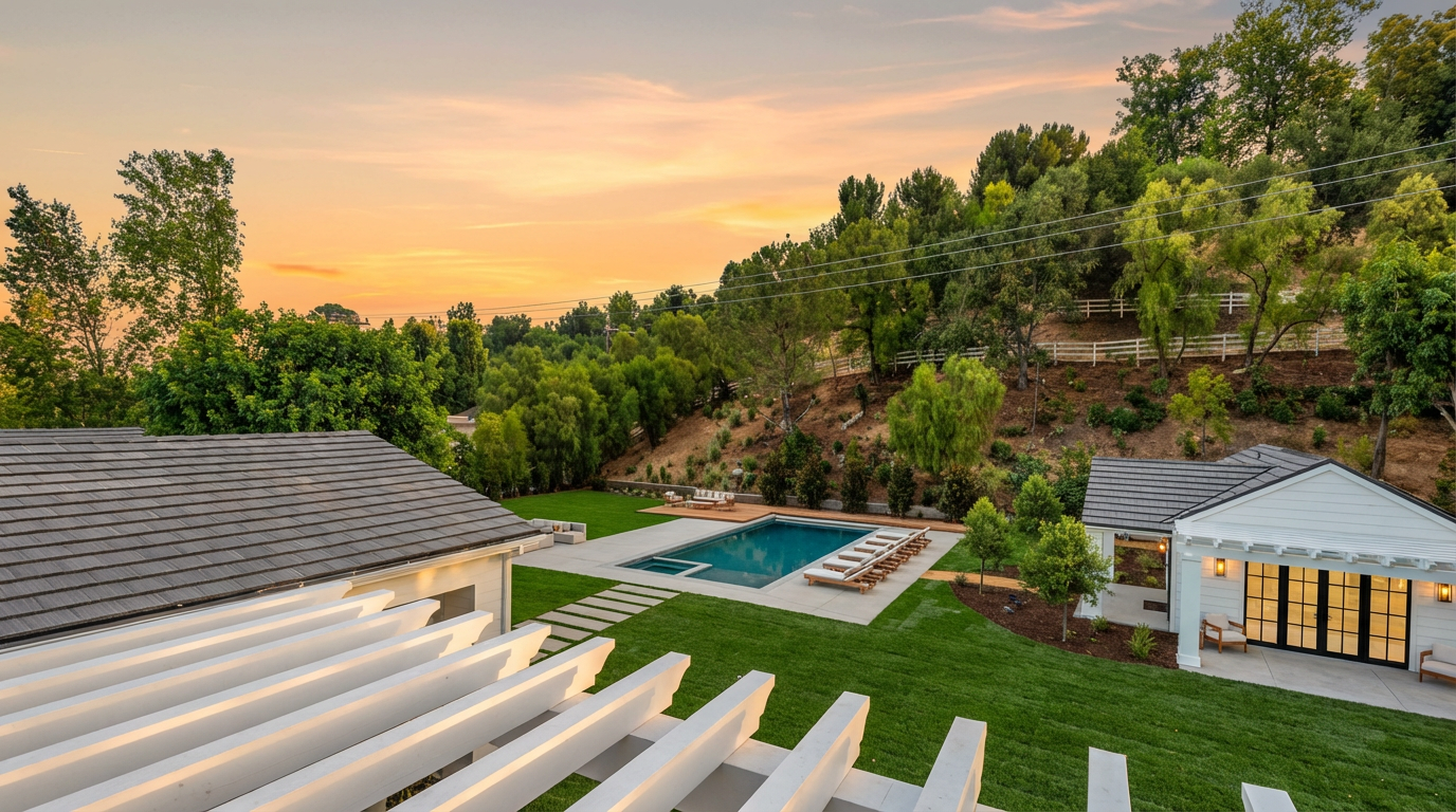 This elevated perspective captures a beautifully landscaped backyard featuring a pristine rectangular swimming pool as the central focal point. The scene includes a lush green lawn, a modern pergola structure in the foreground, and a charming pool house, all set against a backdrop of mature trees and a hillside. The overall impression is one of luxury, tranquility, and high-end outdoor living.