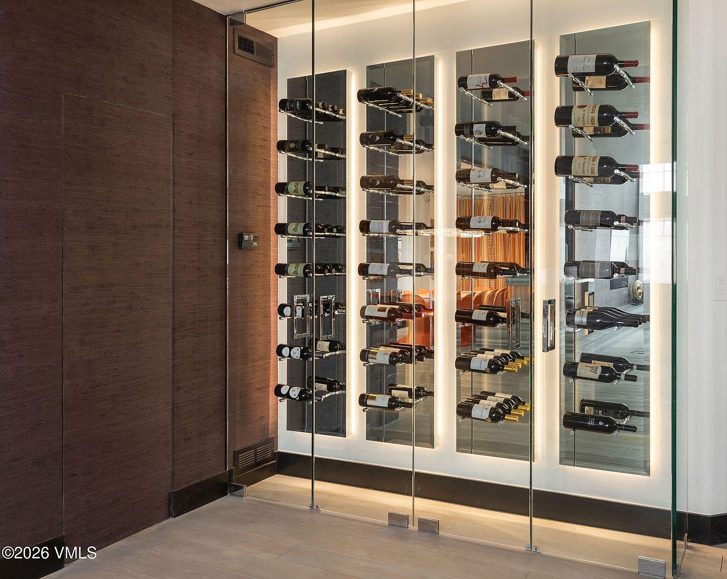 This image showcases a modern wine cellar with a sophisticated design. The wine bottles are displayed on sleek, mirrored racks with integrated lighting, creating an elegant and visually appealing presentation. The cellar is enclosed by glass panels, offering a clear view of the wine collection and adding to the contemporary aesthetic.