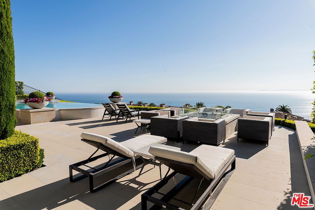 This image showcases a luxurious patio or deck area with stunning ocean views. The space is furnished with modern lounge chairs and outdoor seating arrangements, including a fire pit feature. The design emphasizes relaxation and entertainment, making it an ideal outdoor living space for enjoying the scenic surroundings.