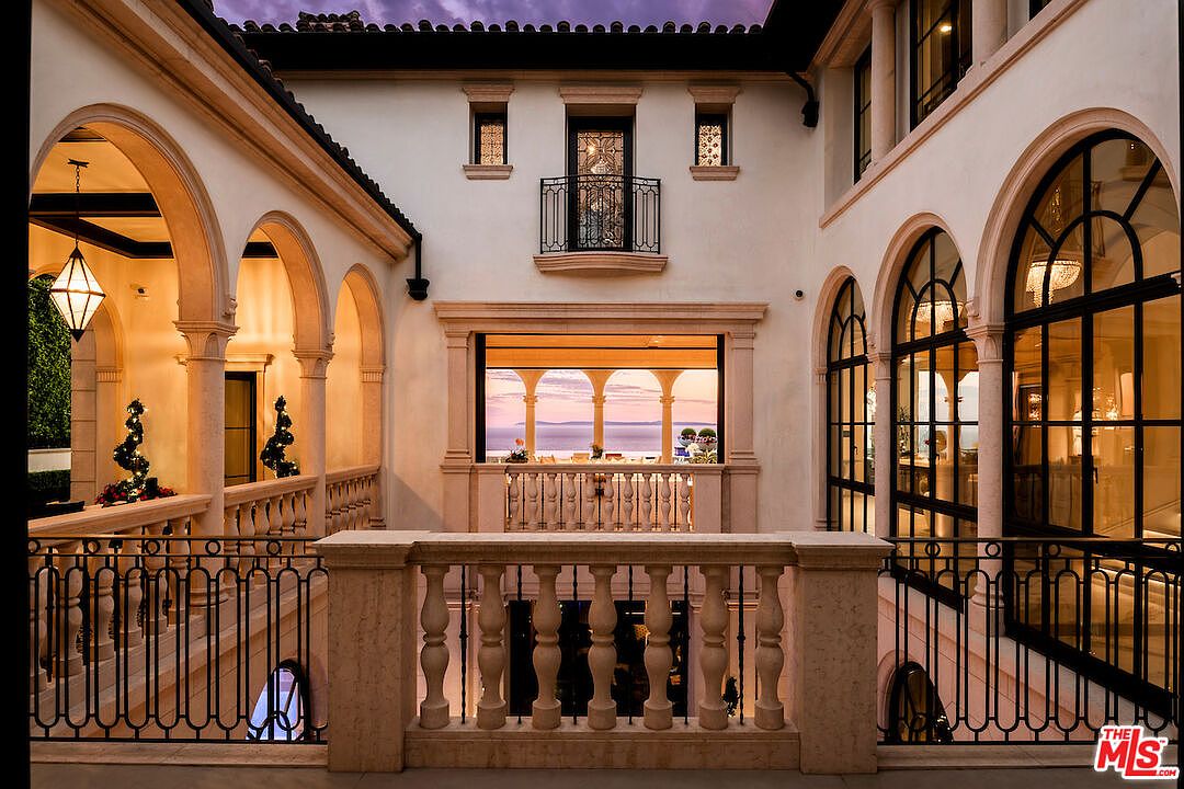 This image showcases a luxurious outdoor space with a multi-level patio or balcony area. The architecture features elegant arches, stone balustrades, and wrought iron railings, creating a sophisticated Mediterranean-style ambiance. The open view reveals a serene ocean vista, enhancing the property's appeal and highlighting its premium location.