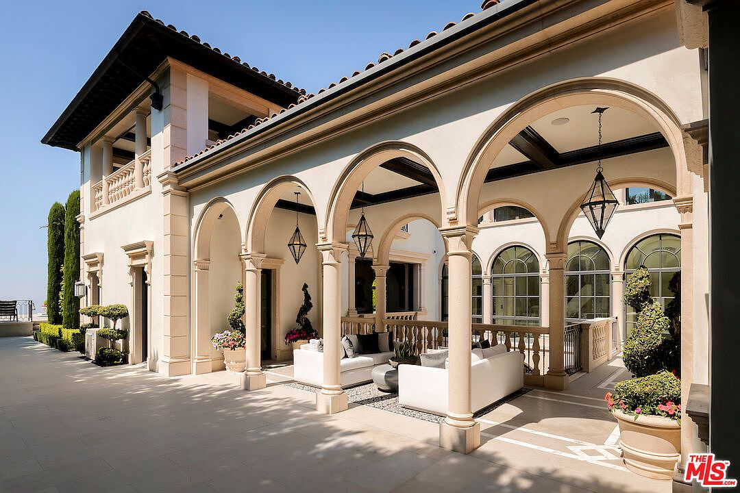 This image showcases a luxurious outdoor patio area with elegant architectural details. The patio features a series of arched columns, creating a covered space furnished with comfortable white sofas and decorative elements. The design exudes sophistication and offers an inviting space for relaxation and entertainment.