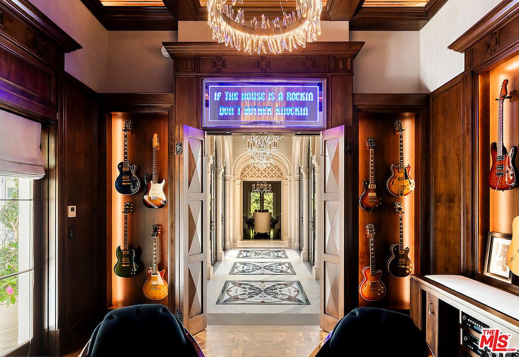 This interior shot showcases a luxurious hallway adorned with guitars displayed in recessed wall niches. The hallway features a marble floor with intricate patterns, leading to a dining area visible through an arched doorway. A neon sign above the doorway adds a modern touch to the otherwise classic and elegant design.