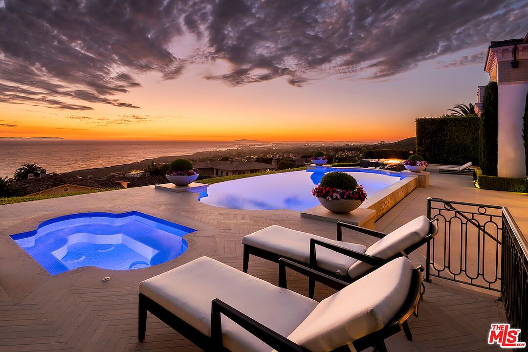 This image showcases a luxurious outdoor pool and spa area at sunset. The infinity pool and separate spa offer stunning ocean views, complemented by elegant lounge chairs and manicured landscaping. The scene exudes relaxation and high-end living, perfect for attracting discerning buyers.