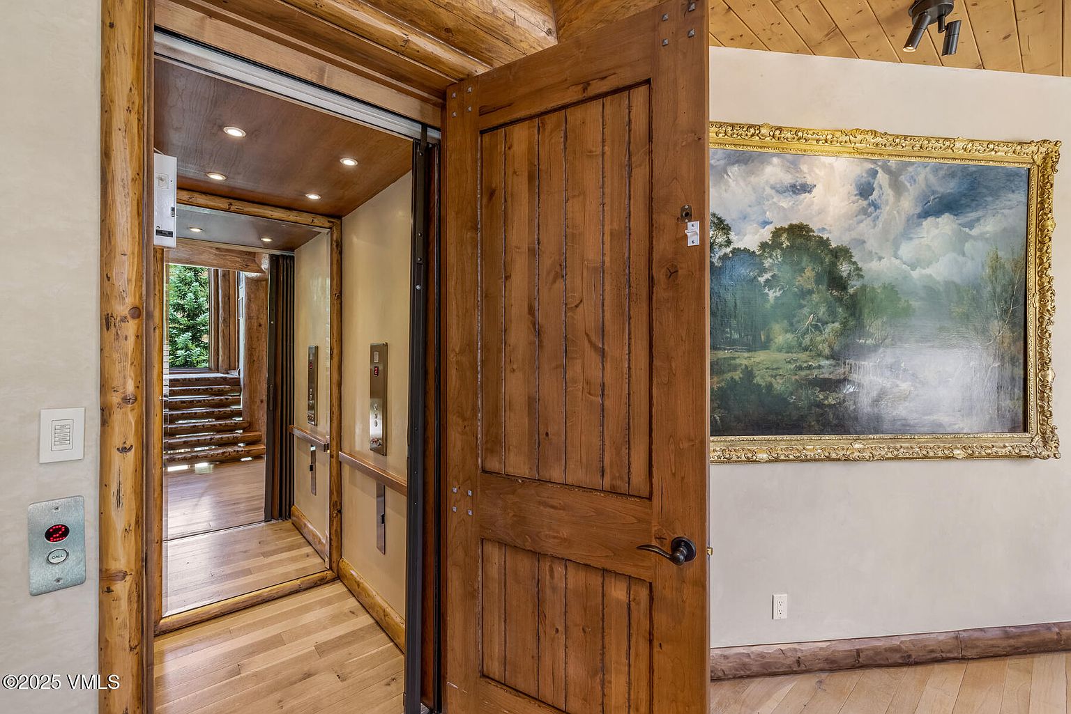 This interior shot showcases a unique elevator within a rustic-style home. The elevator's wooden frame and interior paneling blend seamlessly with the surrounding log cabin architecture. An open wooden door reveals a glimpse of the elevator's interior, while a framed painting adorns the adjacent wall, adding a touch of elegance to the space.