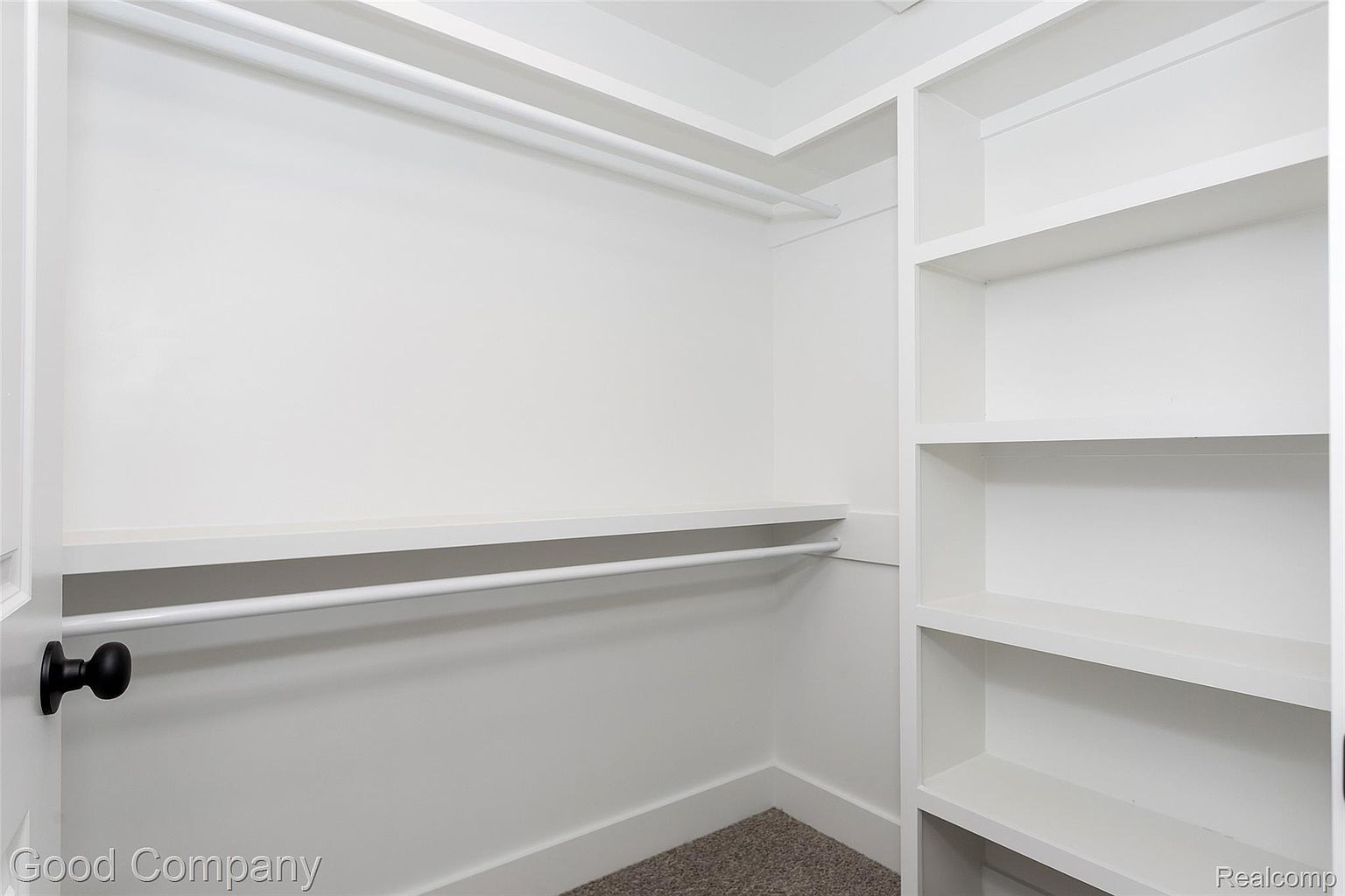 This is a well-organized walk-in closet featuring white shelving and rods for hanging clothes. The closet has a clean and minimalist design, with neutral-colored carpeting. The space appears spacious and functional, offering ample storage.