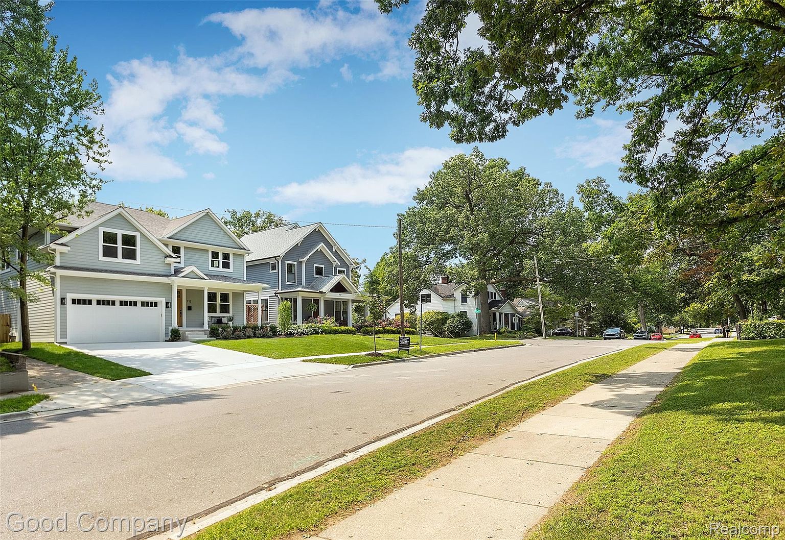 This image showcases the front view of two well-maintained, two-story houses with charming curb appeal. The house on the left features a light gray exterior with a white garage door and a well-manicured lawn, while the house on the right has a darker gray exterior with a welcoming front porch. The street is clean and lined with trees, creating a pleasant neighborhood atmosphere.
