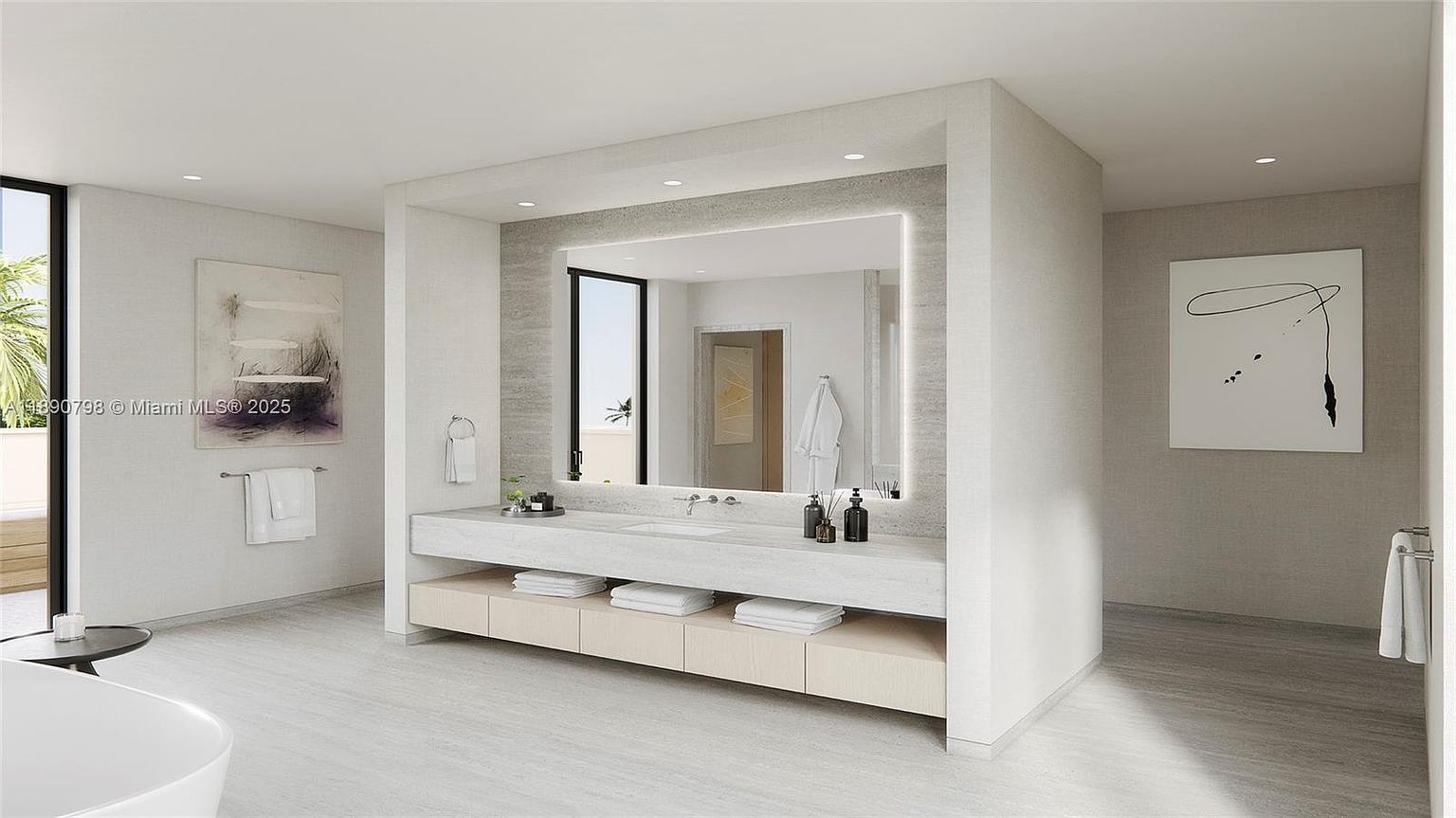 This is a modern primary bathroom featuring a large, illuminated mirror above a long vanity with a light-colored countertop and storage shelves. The walls are a neutral tone, and there is artwork on the walls. The bathroom has a clean, minimalist design with a spa-like atmosphere.