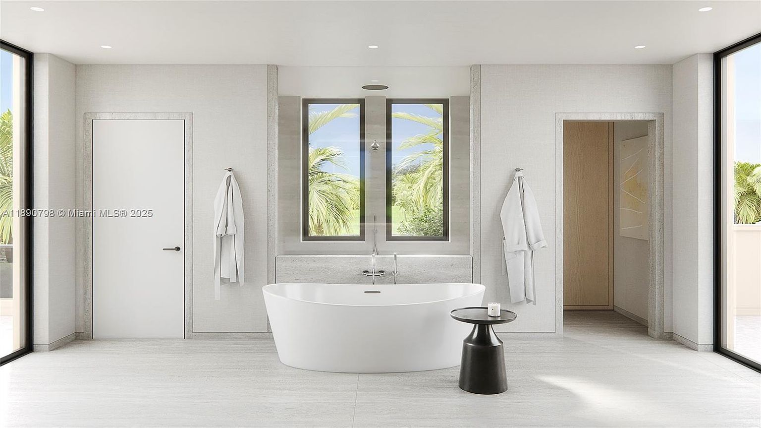 This is a bright and modern primary bathroom featuring a freestanding white bathtub as the focal point, positioned in front of a window with a view of palm trees. The bathroom has a minimalist design with light-colored tile flooring and walls, complemented by a dark side table and matching window frames. Two white robes hang on the walls, adding to the spa-like atmosphere.