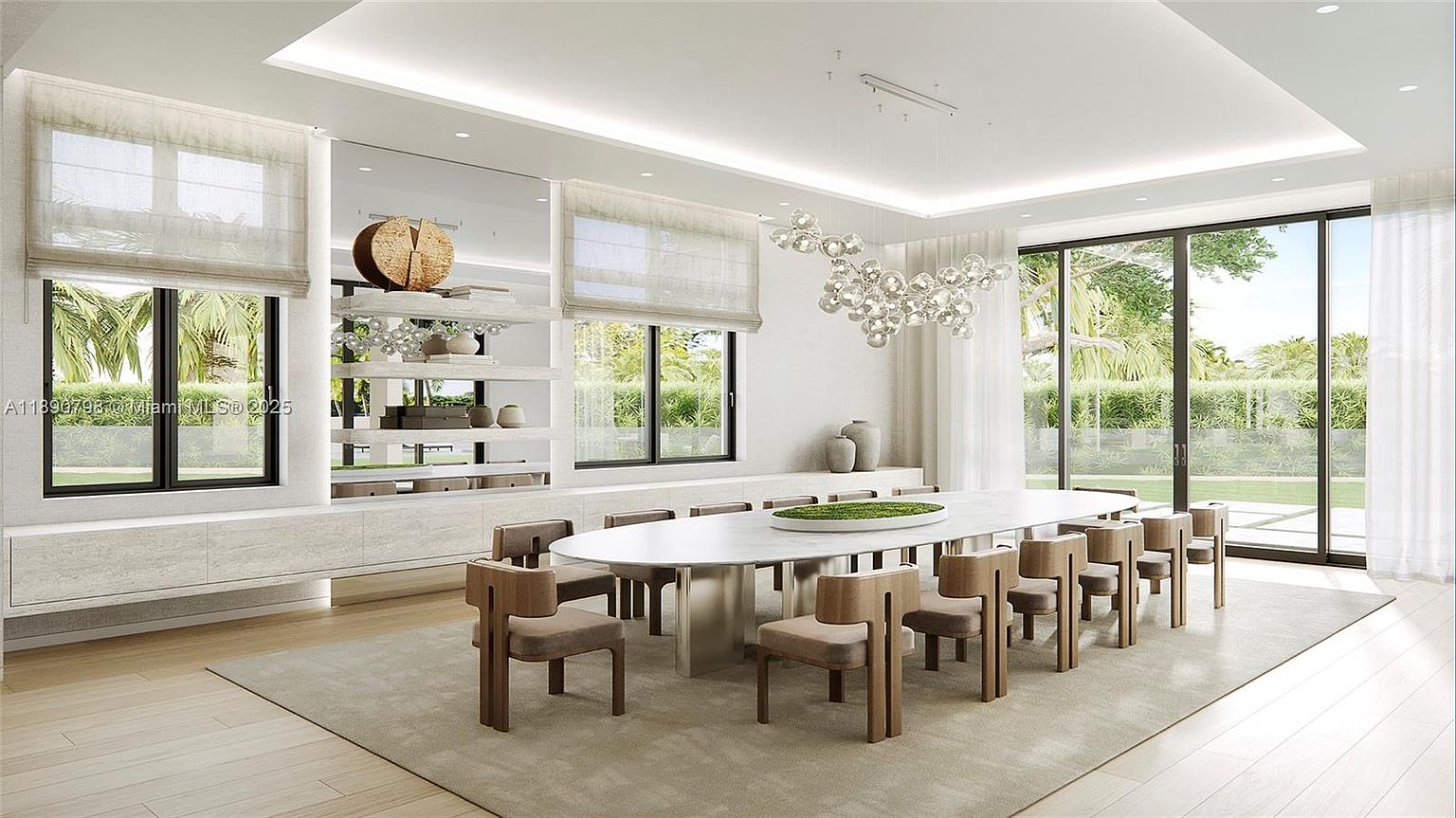 This is a bright and airy dining room featuring a long, oval-shaped dining table with a white top and metallic base, surrounded by modern chairs with wooden frames and upholstered seats. A unique bubble chandelier hangs above the table, and large windows offer views of the lush greenery outside. The room is decorated in a minimalist style with neutral colors, creating a sophisticated and inviting atmosphere.