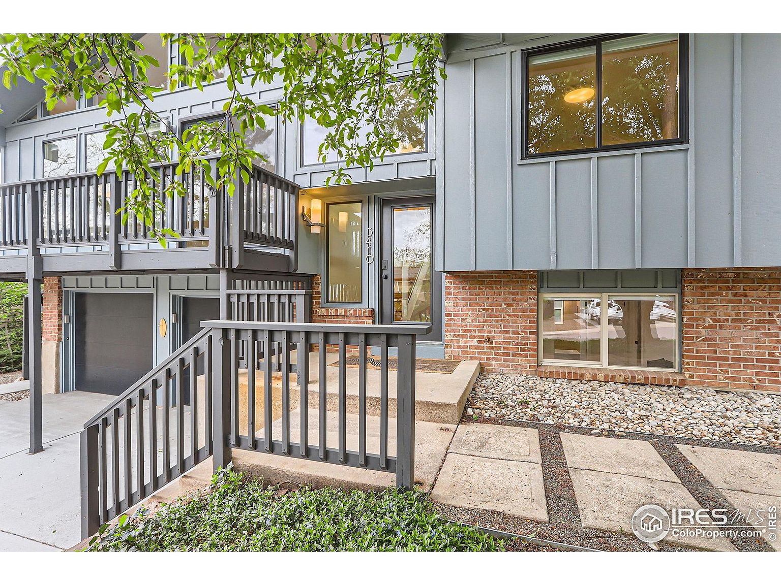 This is an exterior front view of a multi-level home showcasing a unique architectural style. The entryway features a combination of brick and siding, with a set of stairs leading to the front door. A balcony extends from the upper level, adding visual interest and potential outdoor space.