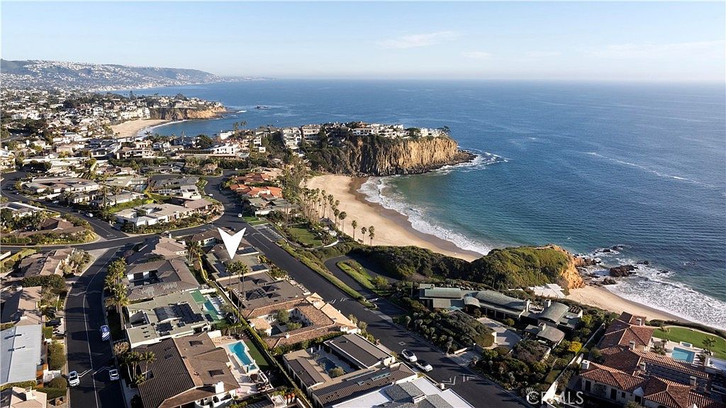 This aerial shot showcases a luxurious coastal neighborhood with stunning ocean views. The homes feature well-maintained landscaping, private pools, and architectural designs that complement the seaside setting. The image captures the proximity to the beach and the overall upscale ambiance of the community.