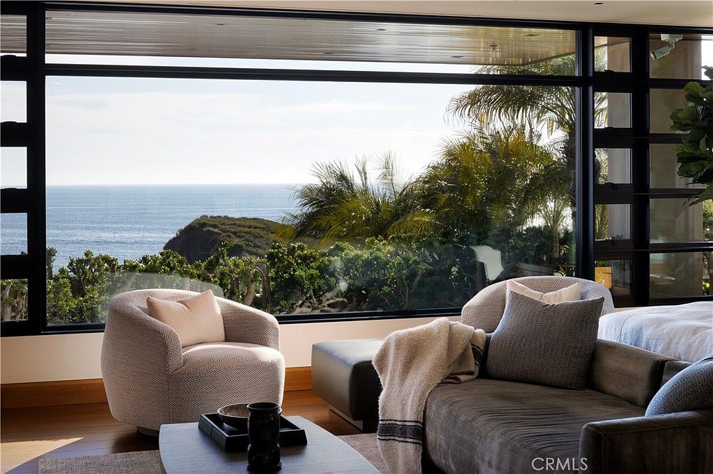 This interior shot showcases a luxurious living room with a stunning ocean view framed by large windows. The room features comfortable seating, including a stylish armchair and a plush sofa, arranged around a coffee table. The design emphasizes natural light and a seamless connection to the outdoor scenery, creating a serene and upscale atmosphere.