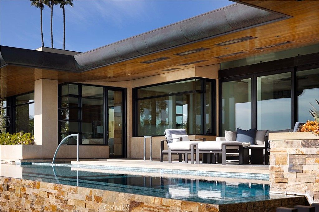 This image showcases a luxurious outdoor living space featuring a modern pool and patio area. The pool is surrounded by stone accents and is adjacent to a covered patio with stylish outdoor furniture. Large windows and doors provide seamless indoor-outdoor flow, enhancing the property's appeal for relaxation and entertainment.