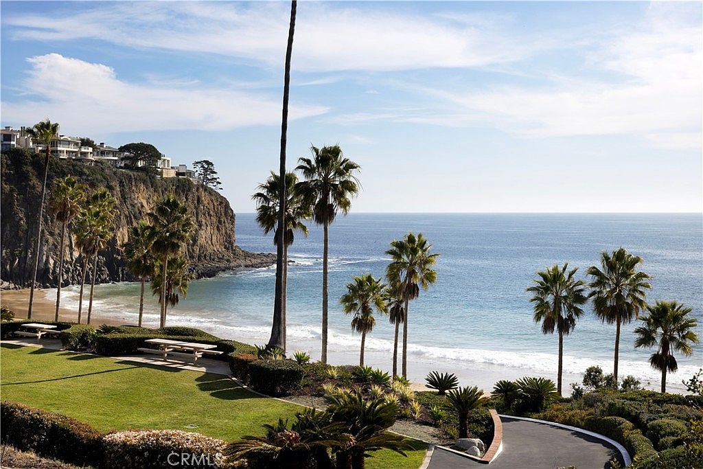 This exterior shot showcases a beautifully landscaped yard overlooking a serene beach. Palm trees dot the landscape, framing the ocean view, while a well-maintained lawn and picnic tables offer a relaxing outdoor space. The image conveys a sense of luxury and tranquility, highlighting the property's desirable location and outdoor amenities.