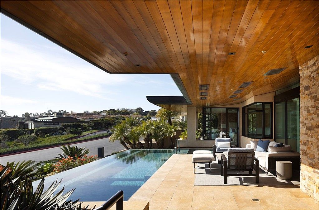This image showcases a luxurious outdoor living space featuring a stunning infinity pool that blends seamlessly with the horizon. The patio area is furnished with comfortable seating, perfect for relaxation, and the wood-paneled ceiling adds a touch of elegance. The design emphasizes a modern aesthetic with clean lines and high-end finishes, creating an inviting and sophisticated atmosphere.