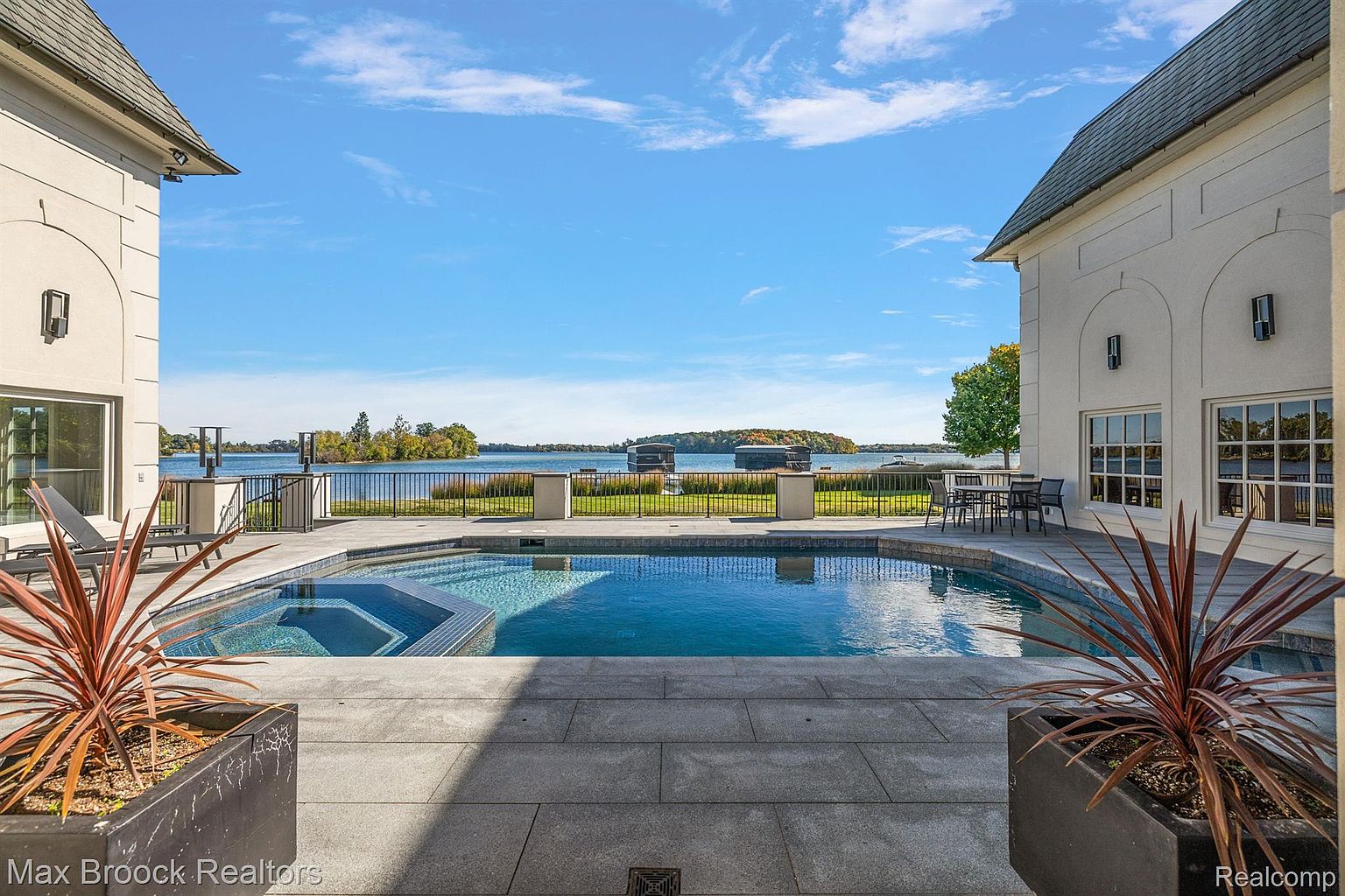 This image showcases a luxurious outdoor pool and spa area, framed by elegant architecture and overlooking a serene lake. The pool features a modern design with a built-in spa, surrounded by a spacious patio. The scene evokes a sense of tranquility and upscale living, perfect for relaxation and entertainment.