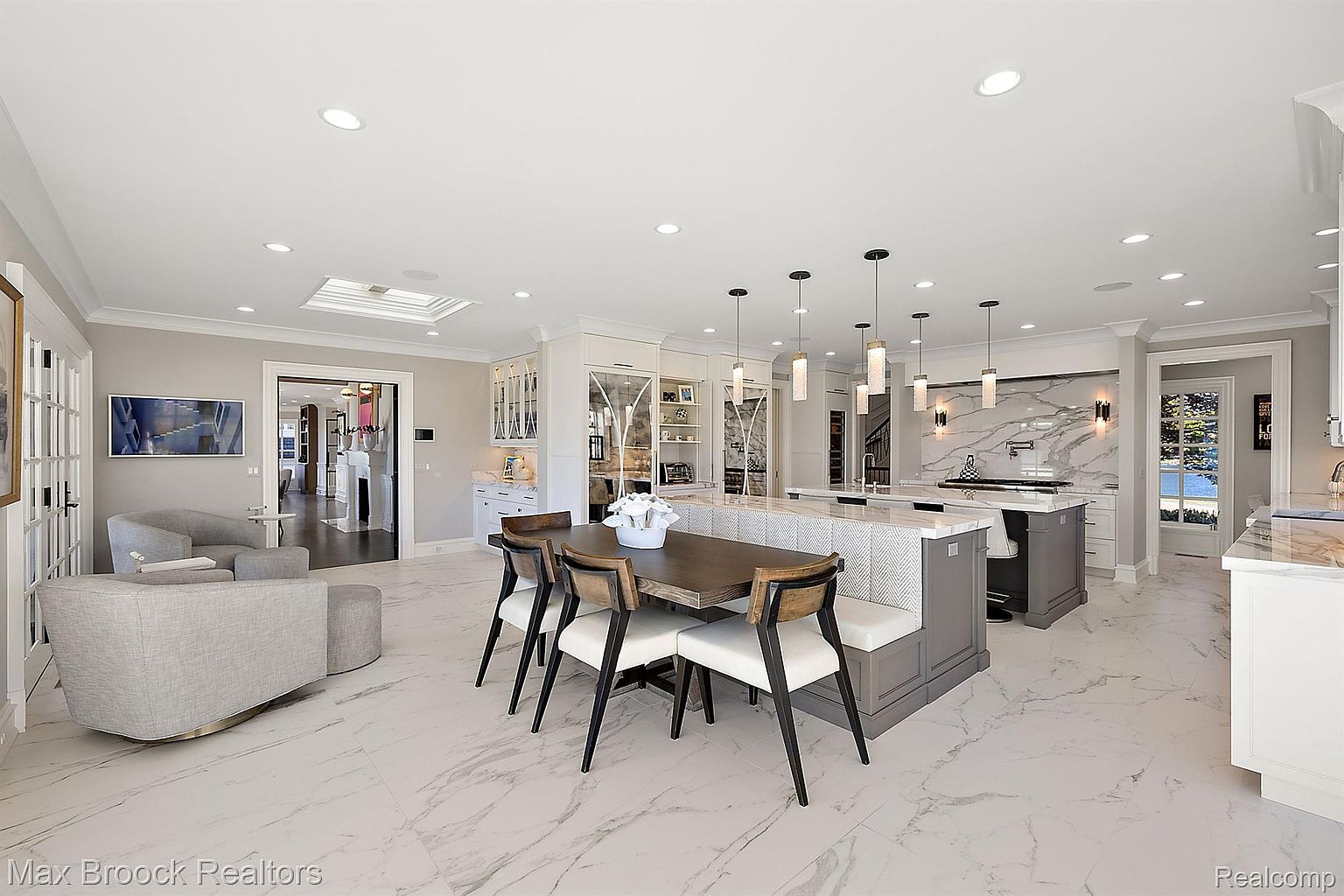 This is a bright and spacious kitchen featuring a large island with seating, a dining table with modern chairs, and high-end appliances. The kitchen boasts marble flooring, custom cabinetry, and stylish pendant lighting. The open layout and neutral color palette create an inviting and luxurious atmosphere.