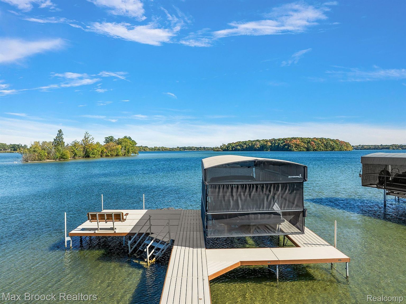 This image showcases a well-maintained dock extending into a serene lake under a clear blue sky. The dock features a boat lift with a protective cover, a seating area, and easy access to the water via steps. The scene evokes a sense of relaxation and waterfront living, highlighting the property's access to recreational water activities.