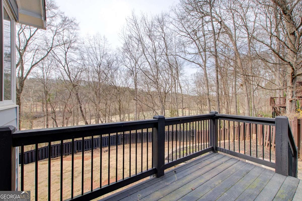 This image captures a wooden deck with black railings, offering an elevated perspective of a wooded backyard. The deck features a weathered finish and provides a clear view of the surrounding trees and a distant grassy field. The scene conveys a peaceful, private outdoor living space perfect for relaxation or entertaining.