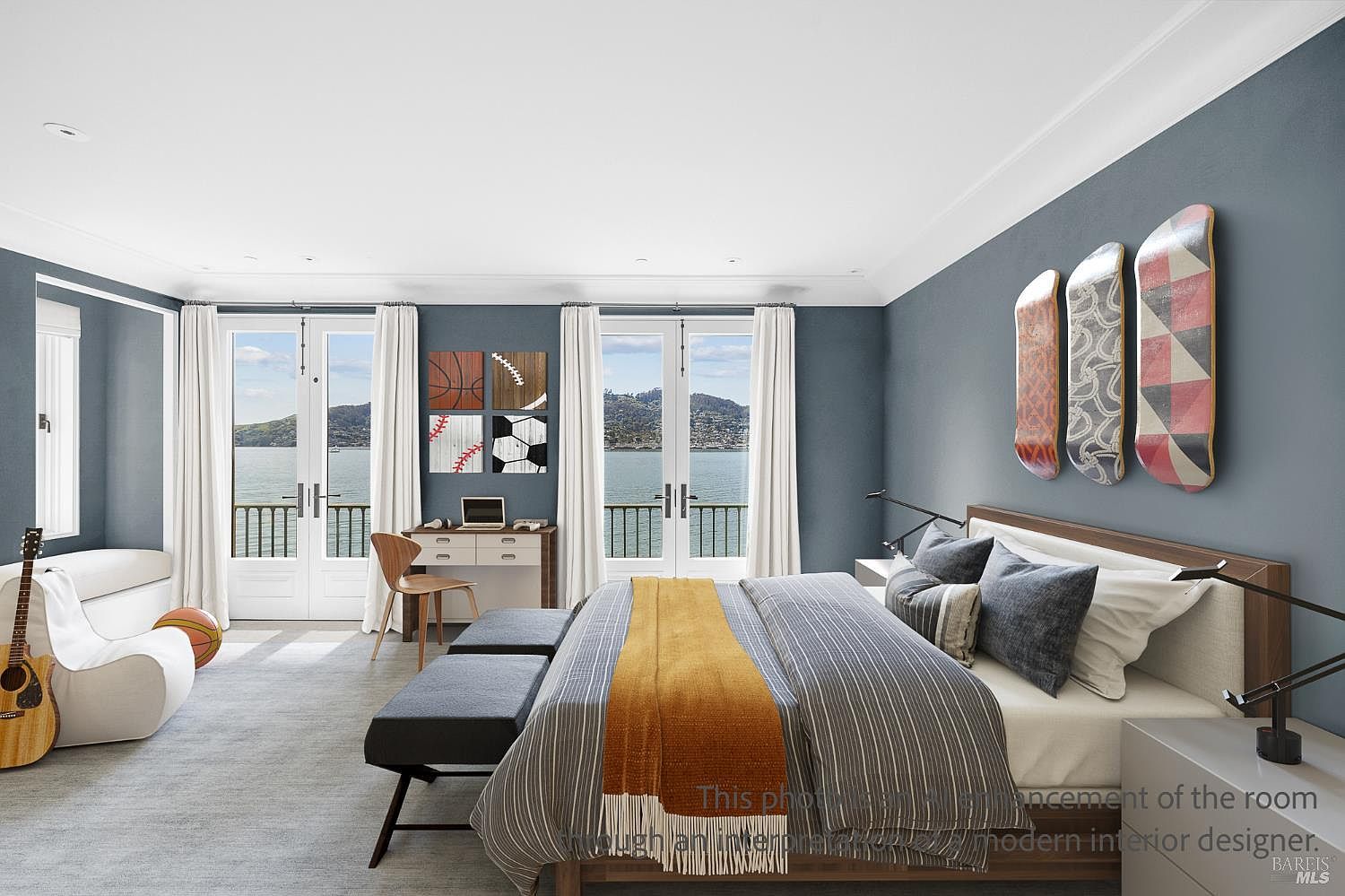 This spacious primary bedroom features a modern aesthetic with a deep blue accent wall adorned with three decorative skateboards. The room is anchored by a large bed with a striped duvet and a warm, textured throw, flanked by two benches at the foot. Large glass doors provide expansive water views and natural light, while a small desk area and a guitar in the corner add a personalized, youthful touch to the sophisticated space.