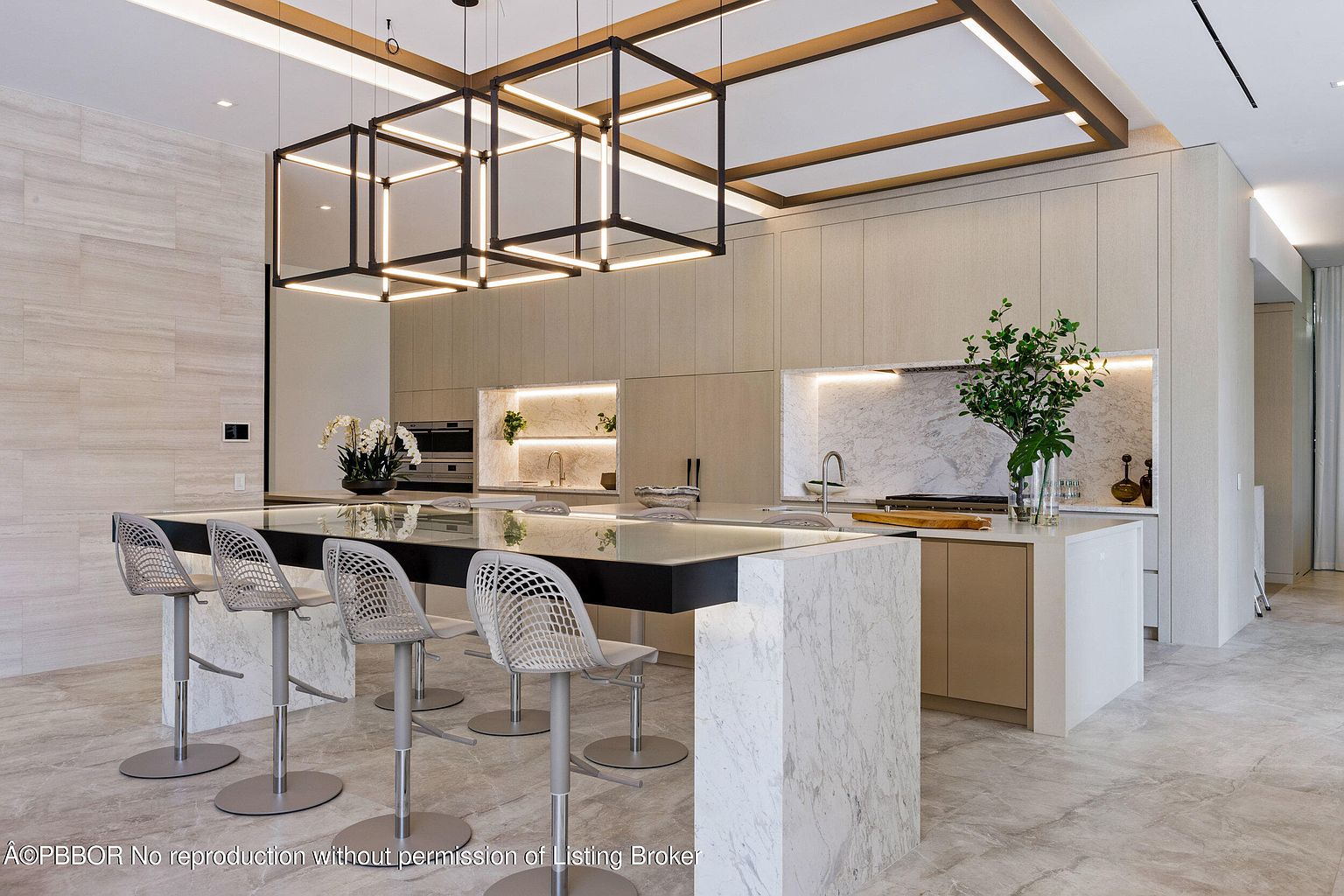 This is a modern, high-end kitchen featuring a large island with seating, sleek cabinetry, and integrated appliances. The lighting is a focal point, with unique geometric fixtures above the island and recessed lighting throughout. The color palette is neutral, creating a sophisticated and inviting space.