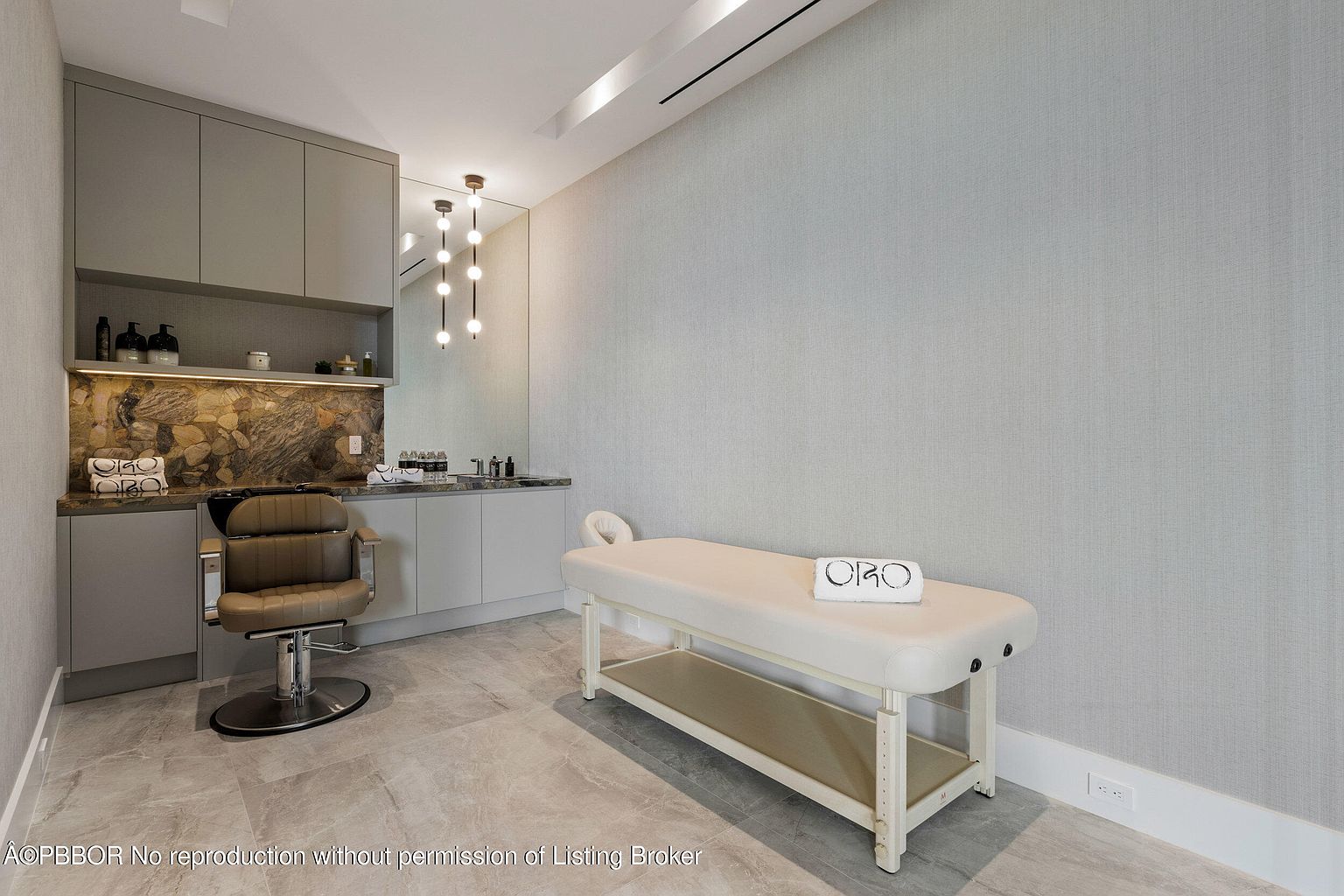 This interior shot showcases a well-appointed spa or treatment room. The room features a massage table with a neatly folded towel, a salon chair, and built-in cabinetry with a countertop and sink area. The color palette is neutral, creating a calming and luxurious atmosphere, suitable for a high-end real estate listing.