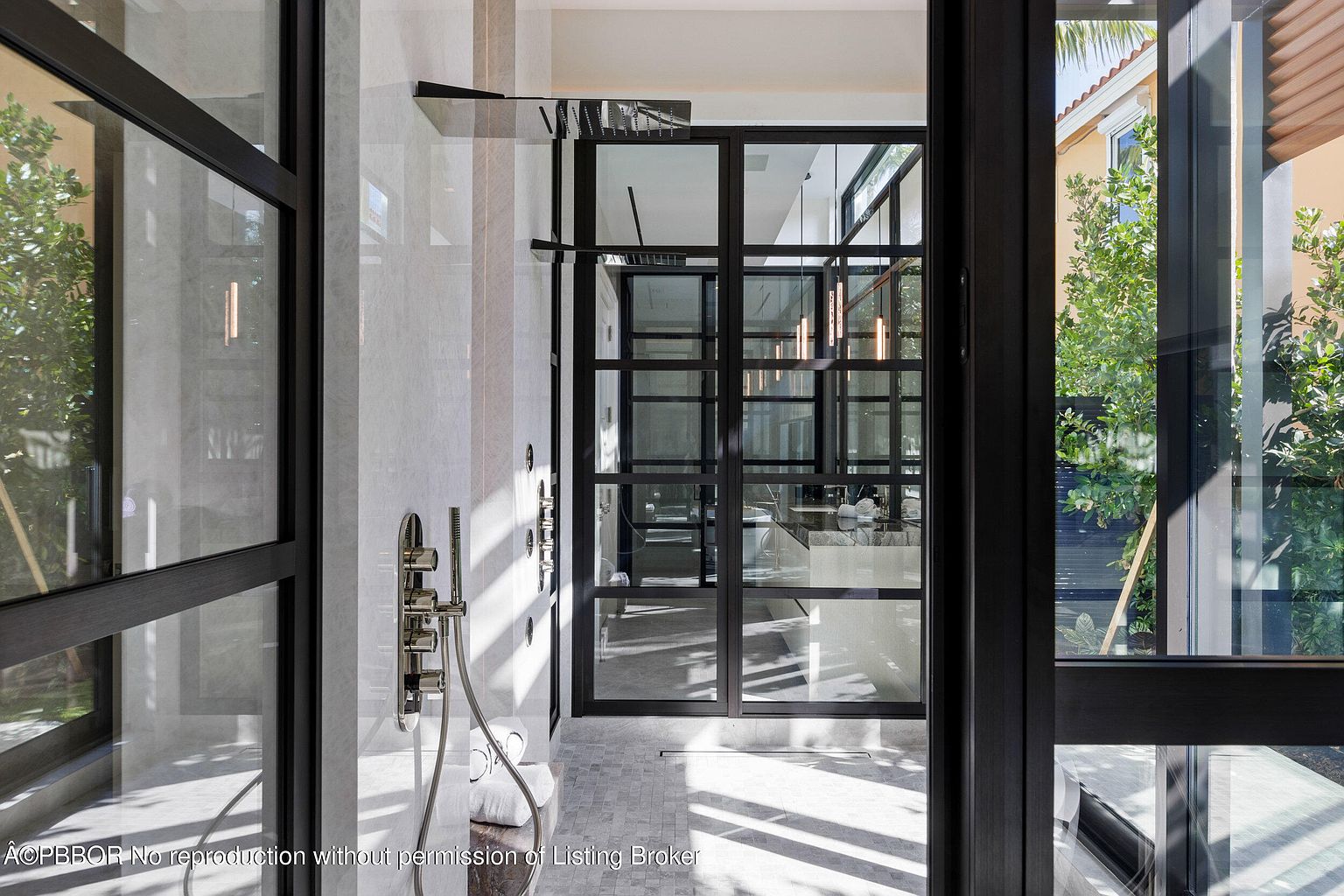 This is a modern primary bathroom featuring a glass-enclosed shower with sleek, chrome fixtures and a rainfall showerhead. The walls are clad in light marble, and the floor is tiled in a mosaic pattern. The bathroom has a contemporary design with clean lines and an open layout, offering a luxurious and spa-like atmosphere.