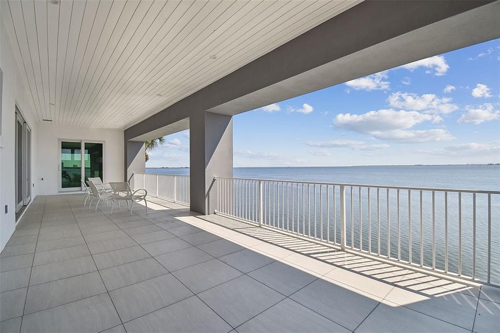 This image showcases a spacious outdoor balcony with a stunning waterfront view. The balcony features a tiled floor, a white railing, and modern outdoor furniture, creating an inviting space for relaxation and entertainment. The open design allows for unobstructed views of the water and sky, enhancing the property's appeal.