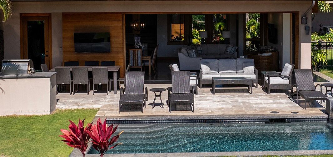 This image showcases a luxurious outdoor living space featuring a pool and patio area. The patio is furnished with comfortable lounge chairs and a dining set, creating an inviting space for relaxation and entertainment. The seamless transition between indoor and outdoor living is emphasized by the open doorway, revealing a glimpse of the interior living area.