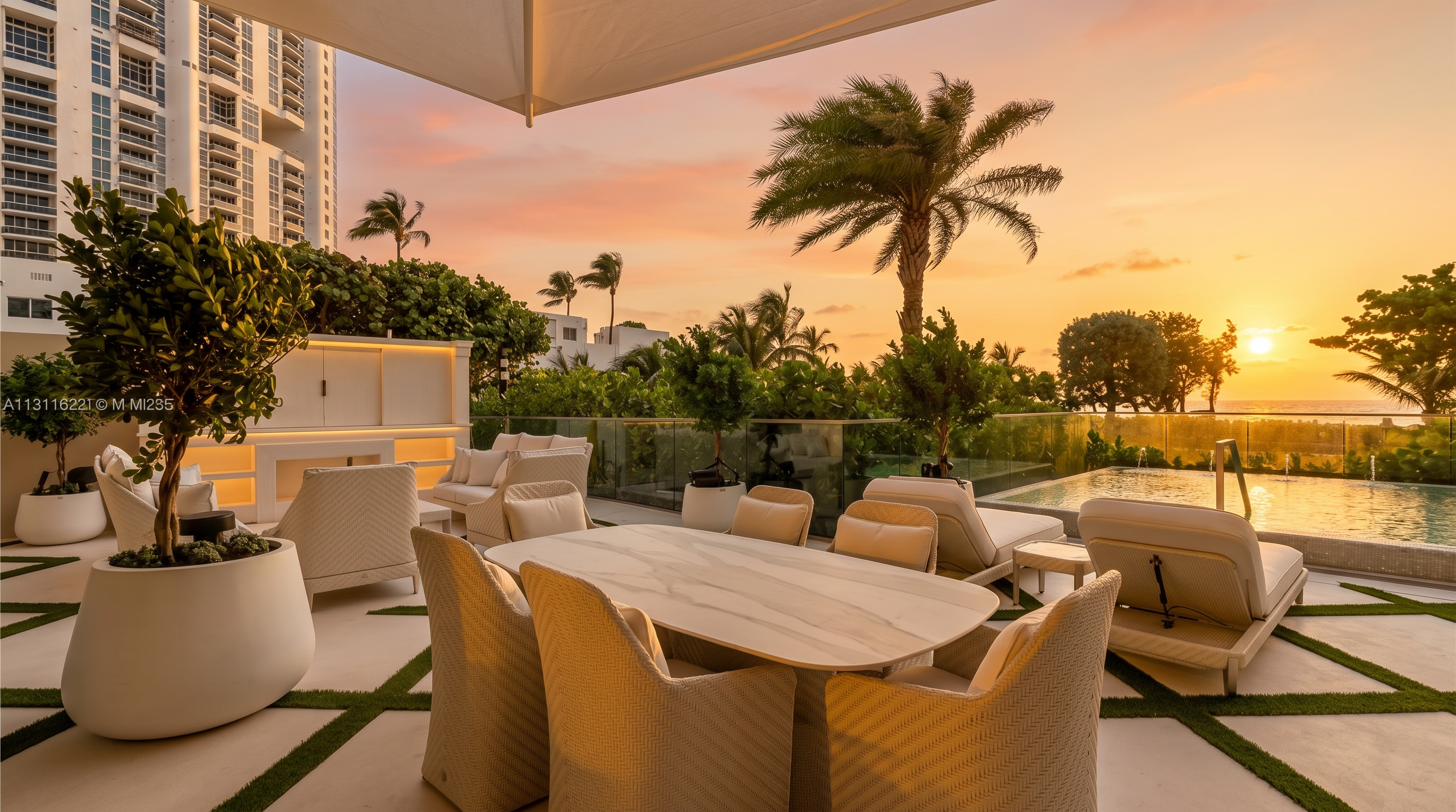 This expansive outdoor terrace features a contemporary dining set with a light-toned stone-topped table and woven chairs, set against a backdrop of lush greenery and a private swimming pool. The space is designed for luxury entertaining, incorporating a glass railing that maintains an open connection to the surrounding landscape and a tall potted tree that adds a natural, sculptural element. The bright, sun-drenched atmosphere and modern furnishings create a sophisticated, resort-like living environment.