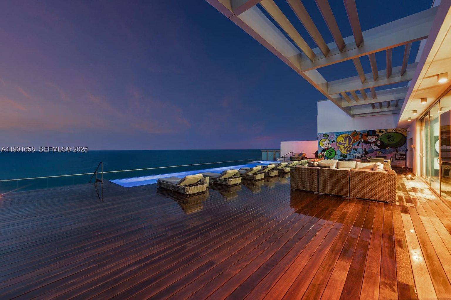 This image showcases a luxurious outdoor patio or deck area, featuring a sleek infinity pool overlooking the ocean. The deck is furnished with modern lounge chairs and a comfortable seating area, complemented by a stylish pergola overhead. The space is designed for relaxation and entertainment, offering stunning views and a sophisticated ambiance.