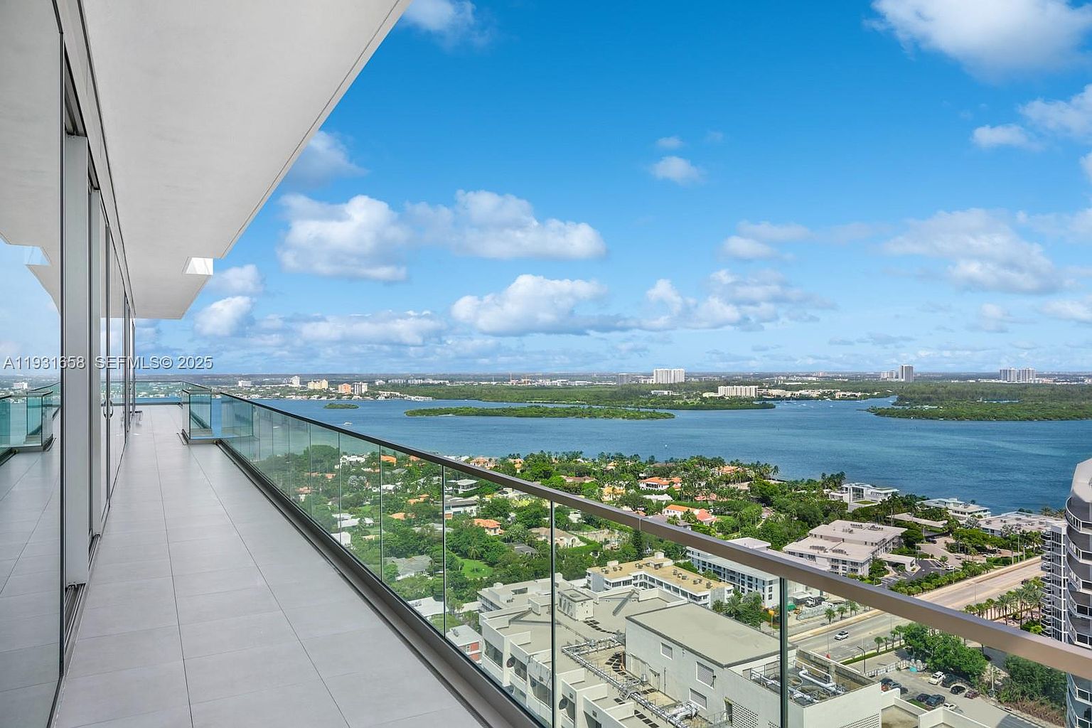 This image showcases a luxurious balcony with a stunning panoramic view of the ocean and cityscape. The balcony features a modern glass railing, providing an unobstructed vista. The scene captures a sense of high-end living and offers a glimpse of the beautiful surroundings, emphasizing the property's prime location and outdoor living space.