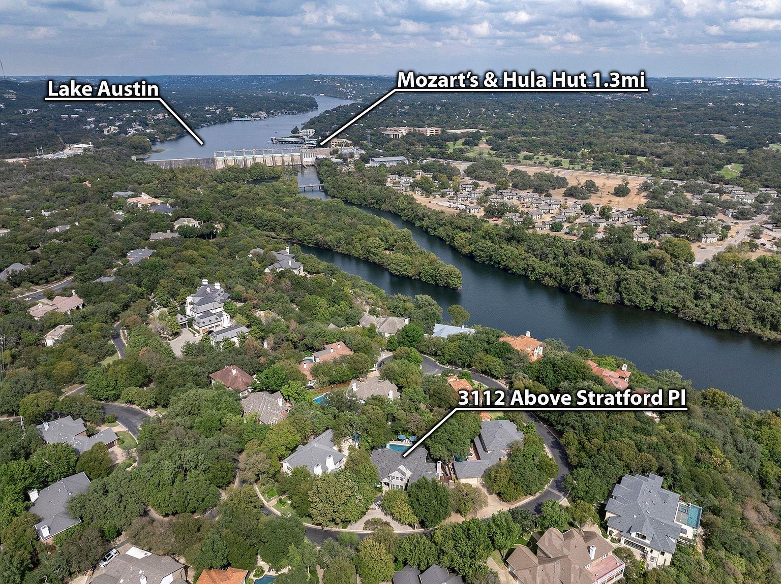 This aerial view showcases a luxurious residential area nestled amidst lush greenery and waterways. The homes feature a variety of architectural styles, with many boasting pools and well-manicured yards. The proximity to Lake Austin and Mozart's & Hula Hut adds to the appeal of this upscale neighborhood, offering both natural beauty and convenient access to local attractions.