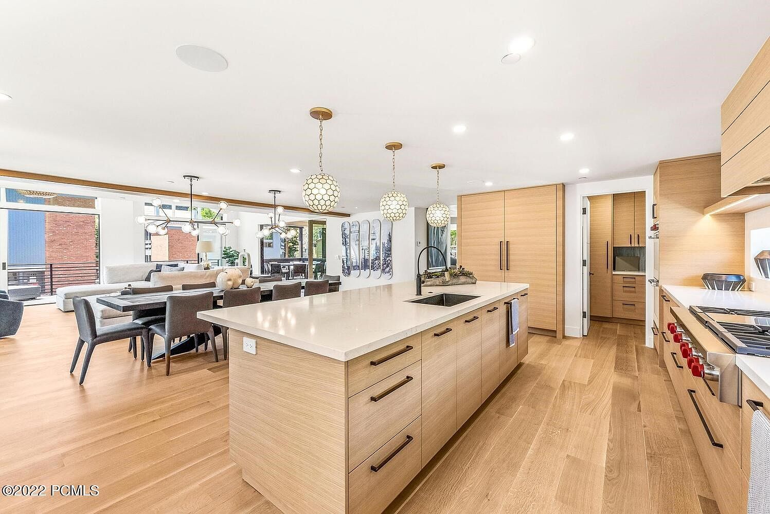 This is a bright and modern kitchen with light wood cabinetry and a large island with a white countertop. The kitchen seamlessly flows into the dining and living areas, creating an open and inviting space. The perspective is from a wide angle, showcasing the kitchen island and the adjacent dining area.