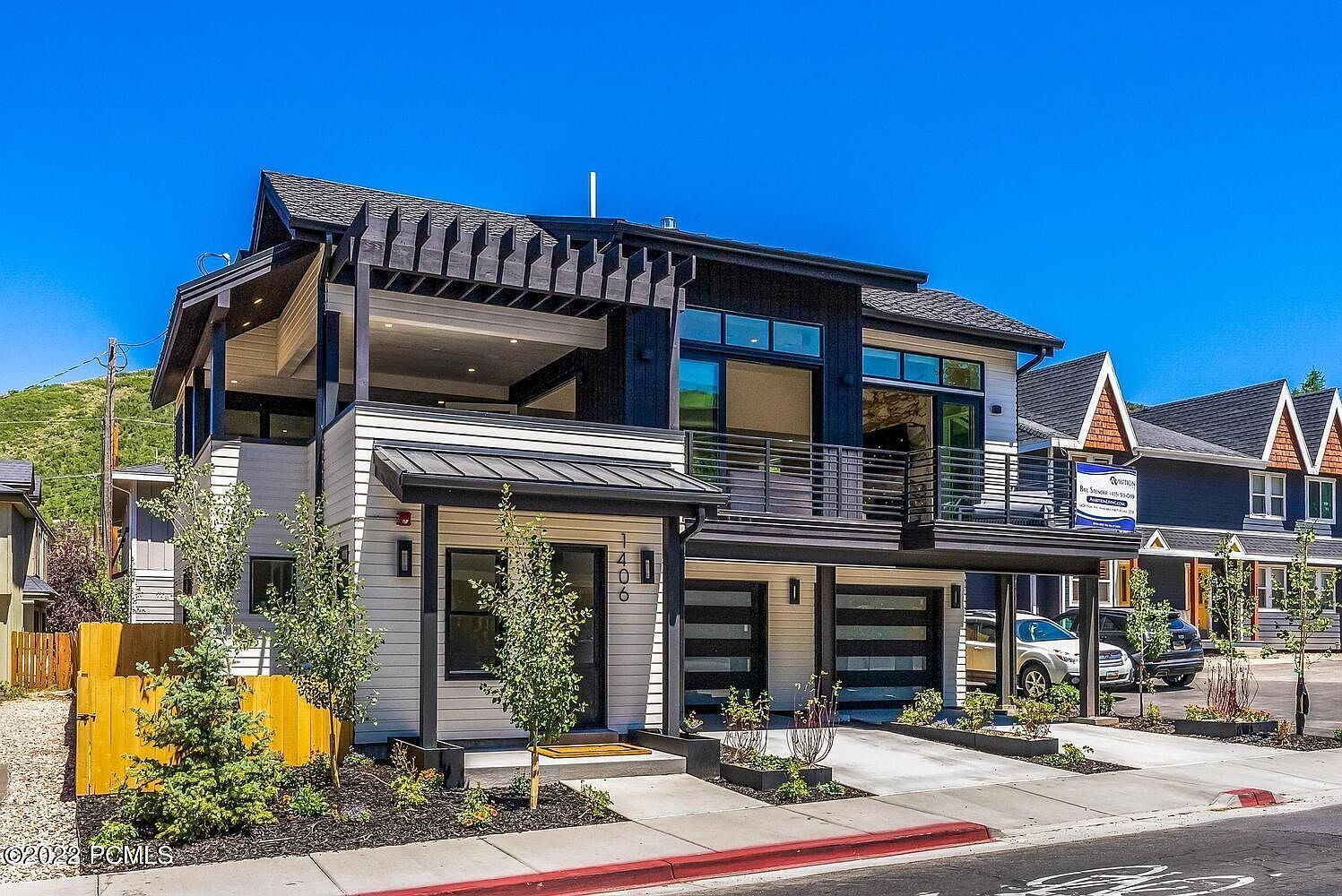 This is a front view of a modern two-story home with a striking black and white color scheme. The house features a covered balcony, a two-car garage with modern glass panel doors, and well-maintained landscaping. The architectural style is contemporary with clean lines and a mix of materials, creating a sophisticated and inviting curb appeal.