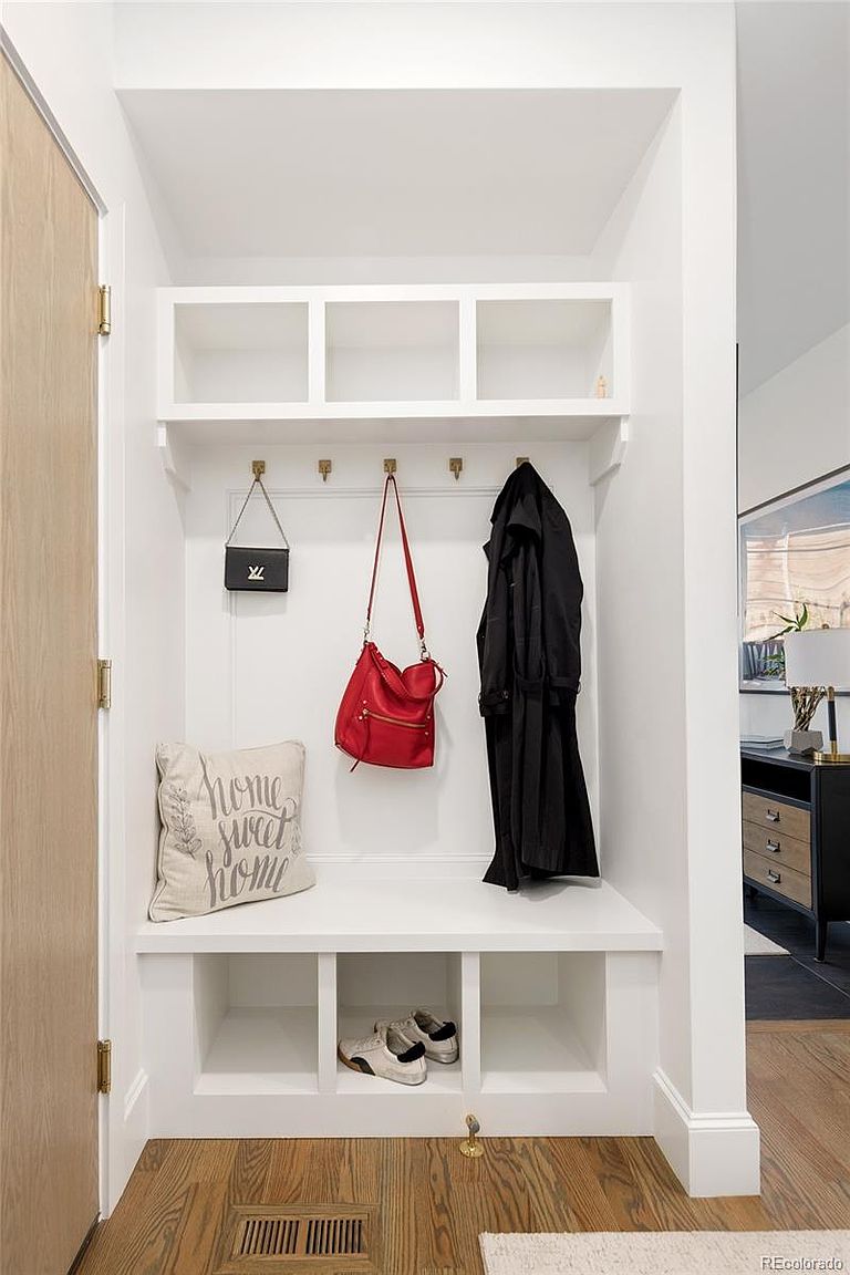 This interior shot showcases a well-organized entryway with a built-in storage unit. The unit features open shelving, hooks for hanging items, and a bench seat with additional storage underneath. A neutral color palette and clean lines contribute to a modern and inviting atmosphere, perfect for a functional and stylish home.