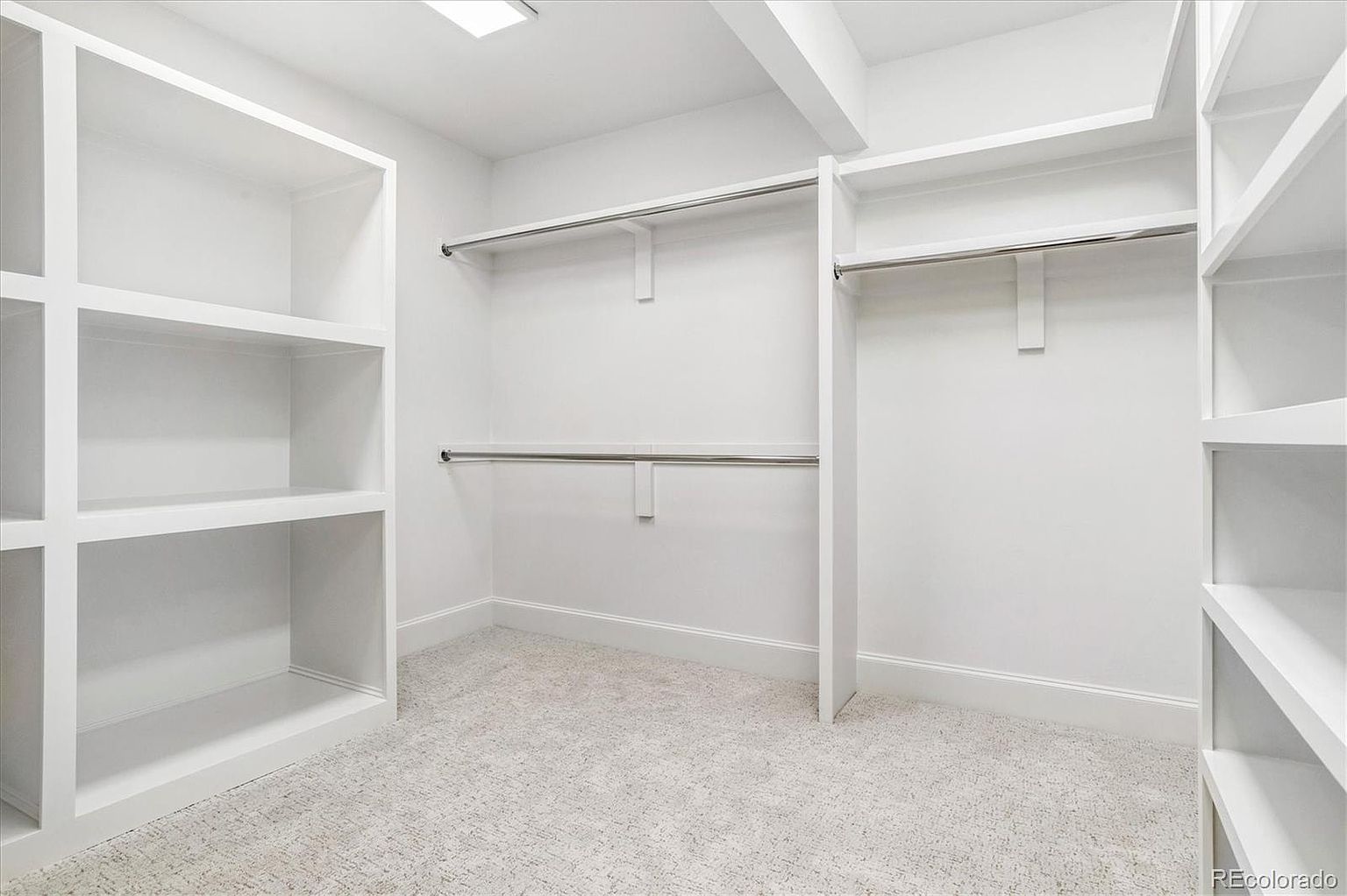 This is a well-organized walk-in closet featuring white shelving and hanging rods. The closet is brightly lit and appears spacious, with neutral carpeting. The design emphasizes functionality and storage capacity, making it an attractive feature for potential buyers.