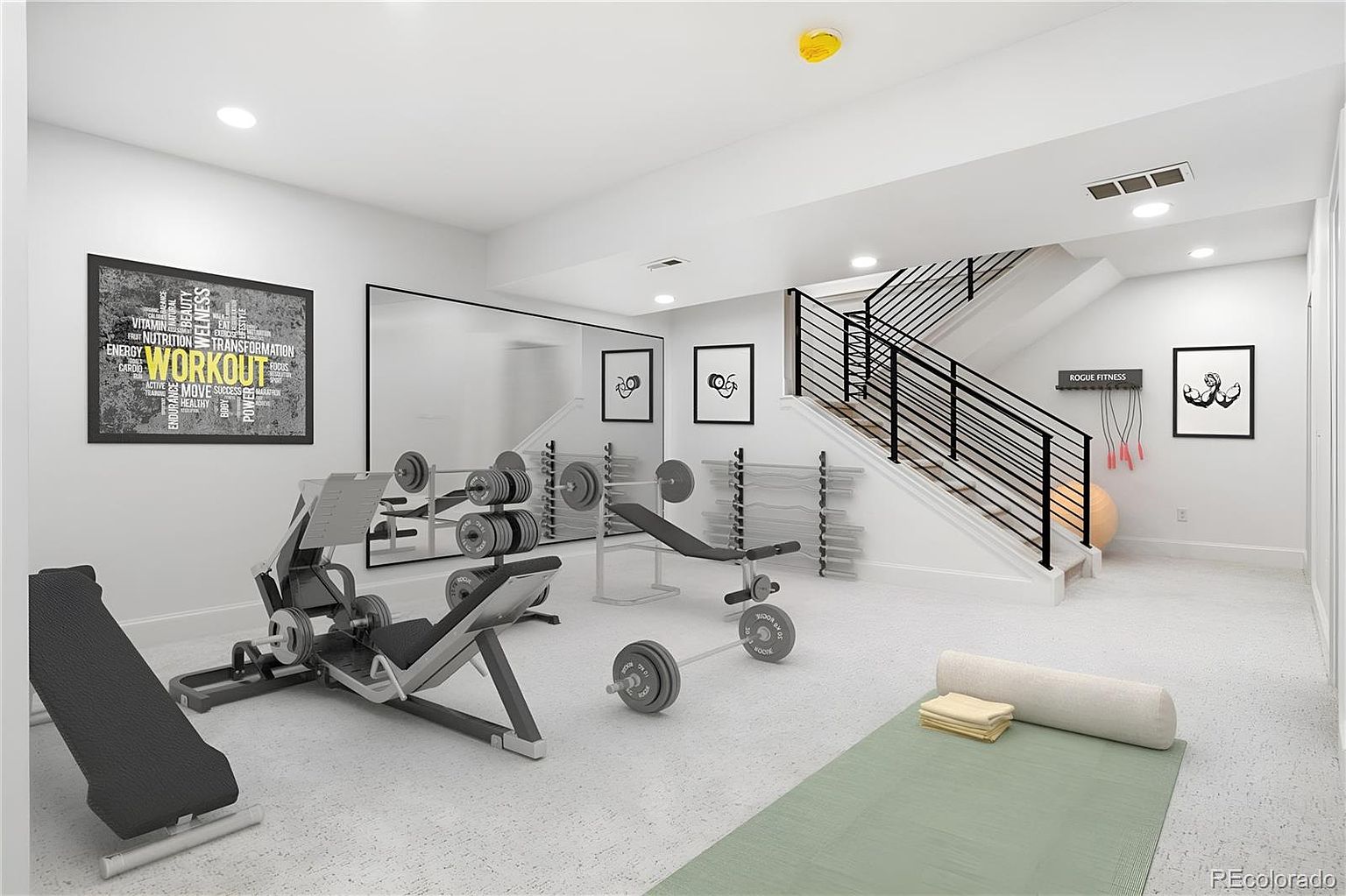 This is a well-equipped home gym featuring various weightlifting machines, barbells, and a yoga mat. The room has a clean and modern aesthetic with white walls, a large mirror, and framed artwork. A staircase with black railings adds architectural interest to the space.