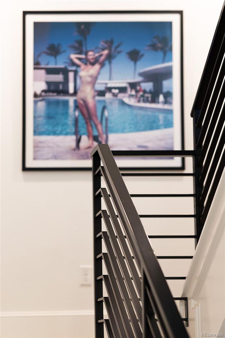 The image showcases a modern staircase with black metal railings and white walls. A framed photograph of a woman by a pool hangs on the wall, adding a touch of elegance and art to the space. The focus is on the clean lines and contemporary design of the staircase, creating a sophisticated and inviting atmosphere.