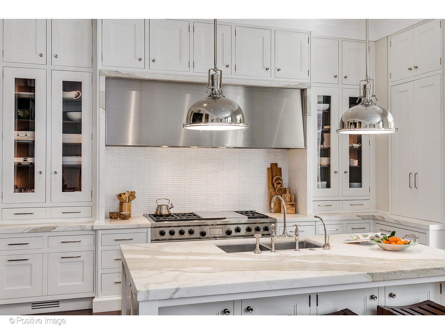 This is a bright and elegant kitchen featuring white cabinetry, marble countertops, and stainless steel appliances. The kitchen island provides ample workspace, and pendant lights illuminate the area. The overall design is sophisticated and functional, perfect for a modern home.