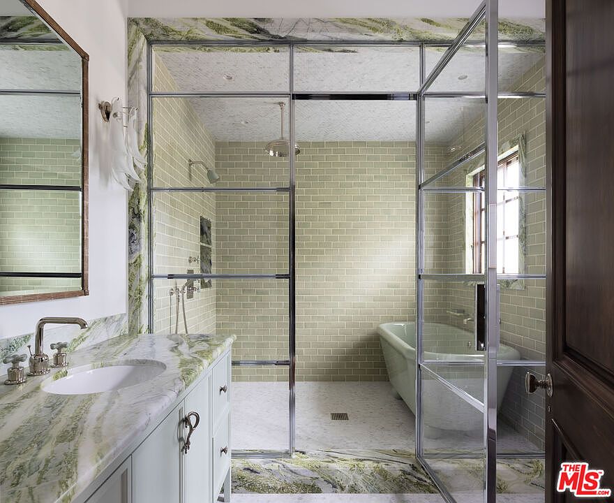 This elegant bathroom features a wet room design with a glass-enclosed shower area that also houses a freestanding soaking tub. The space is accented by striking green-veined stone surfaces on the vanity countertop and framing the shower enclosure, complemented by light-toned subway tile walls. A polished chrome faucet and shower fixtures add a refined touch to this sophisticated, spa-like retreat.