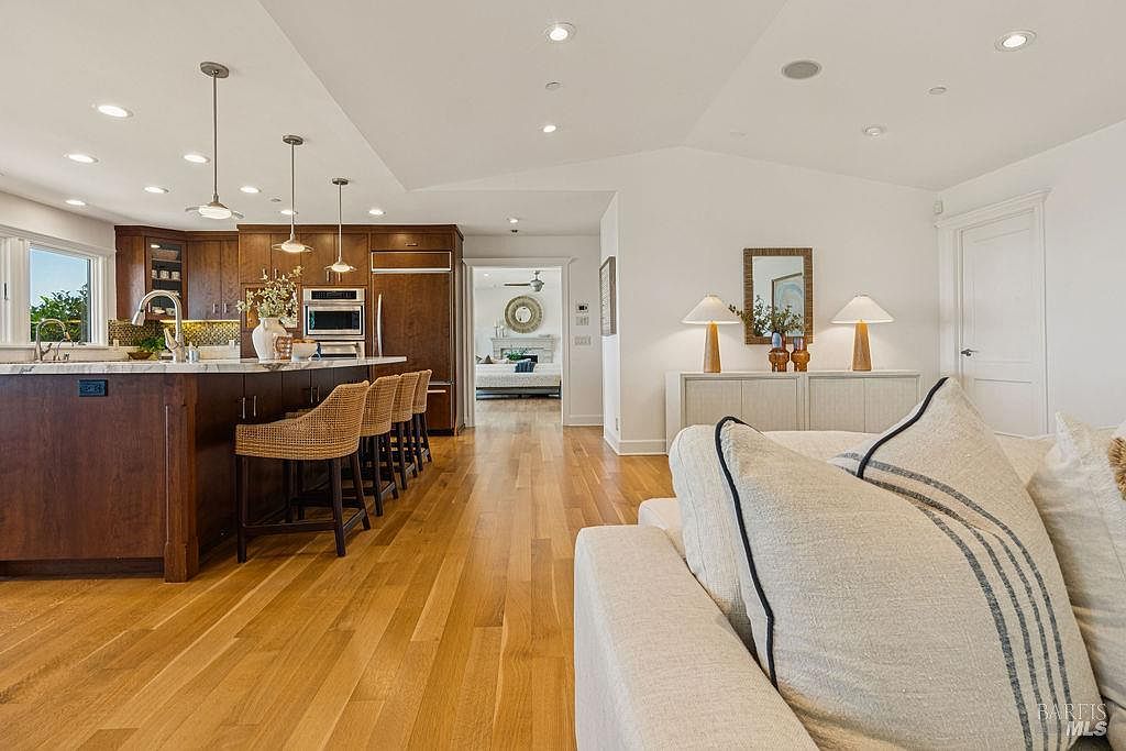 This interior shot showcases a modern kitchen seamlessly flowing into a living area. The kitchen features dark wood cabinetry, a large island with seating, and stainless steel appliances. The living area is bright and airy, with a comfortable sofa and tasteful decor, creating an inviting and open living space.